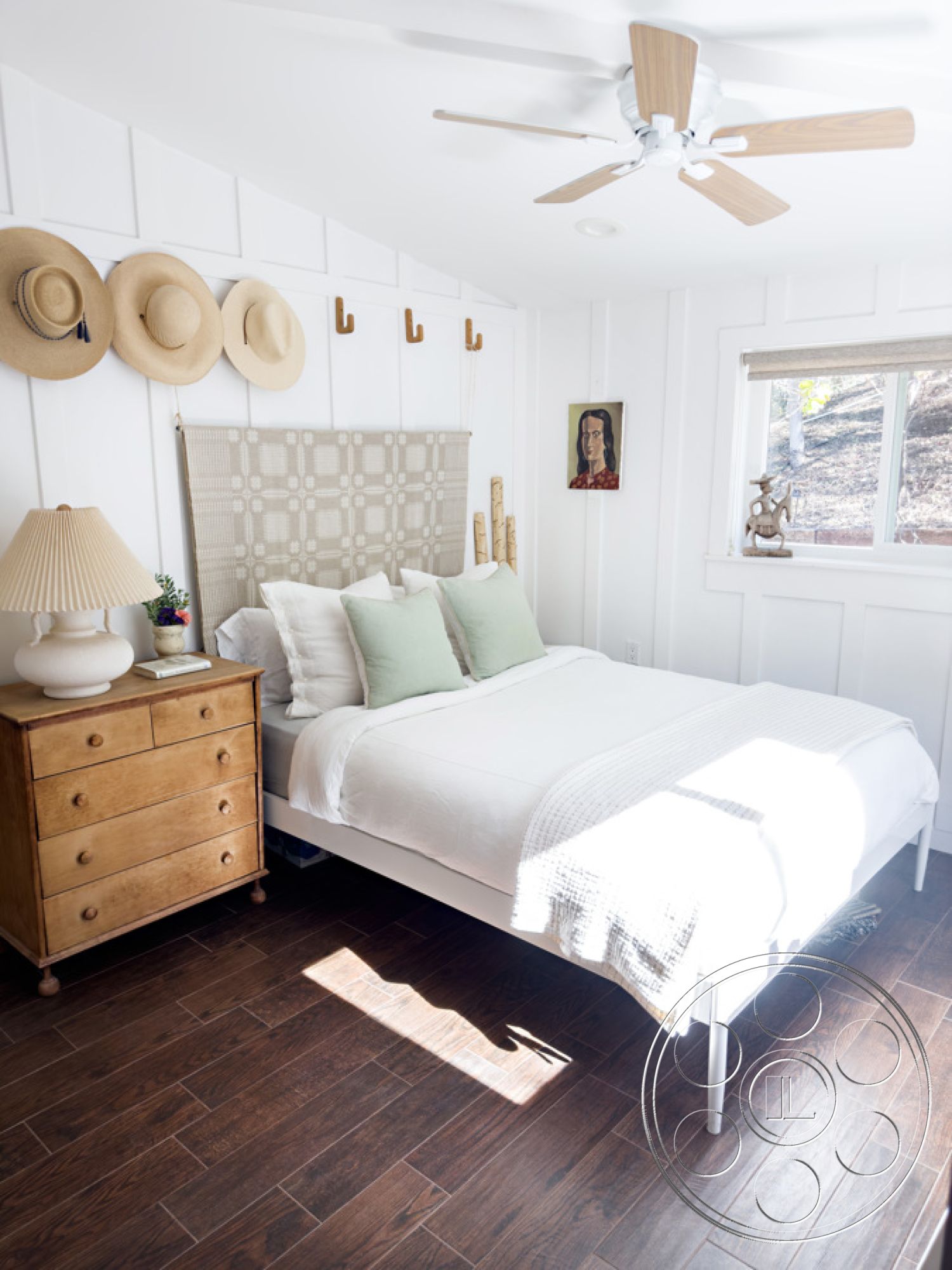 Ranch 33 - decorative wall art, natural light from window, modern ceiling fan, cozy bedroom setting, hardwood bedroom floors, white painted walls interior, shiplap wall treatment, minimalist bedroom design, textured throw blanket on bed, traditional bed with upholstered headboard, brown wooden dresser, soft lighting from bedside lamp, earthy green accent pillows, stylish coat hooks