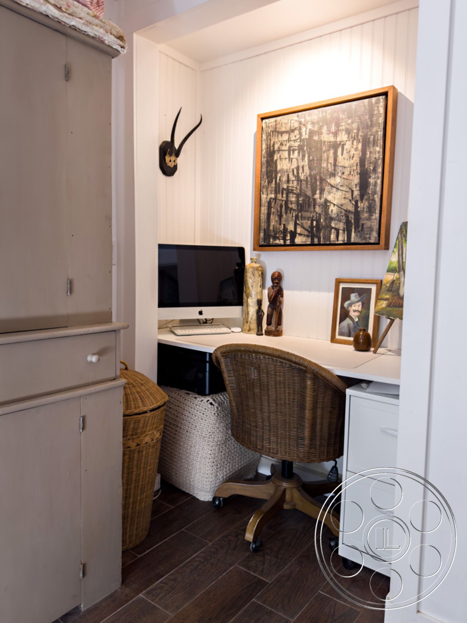 Ranch 33 - bright natural light, dark hardwood flooring, woven rattan chair, minimalist decor style, interior home office, decorative wooden sculptures, white shiplap wall treatment, custom built-in storage cabinet, modern desktop computer setup, textured woven storage basket, framed artwork with abstract design, simple white desk surface