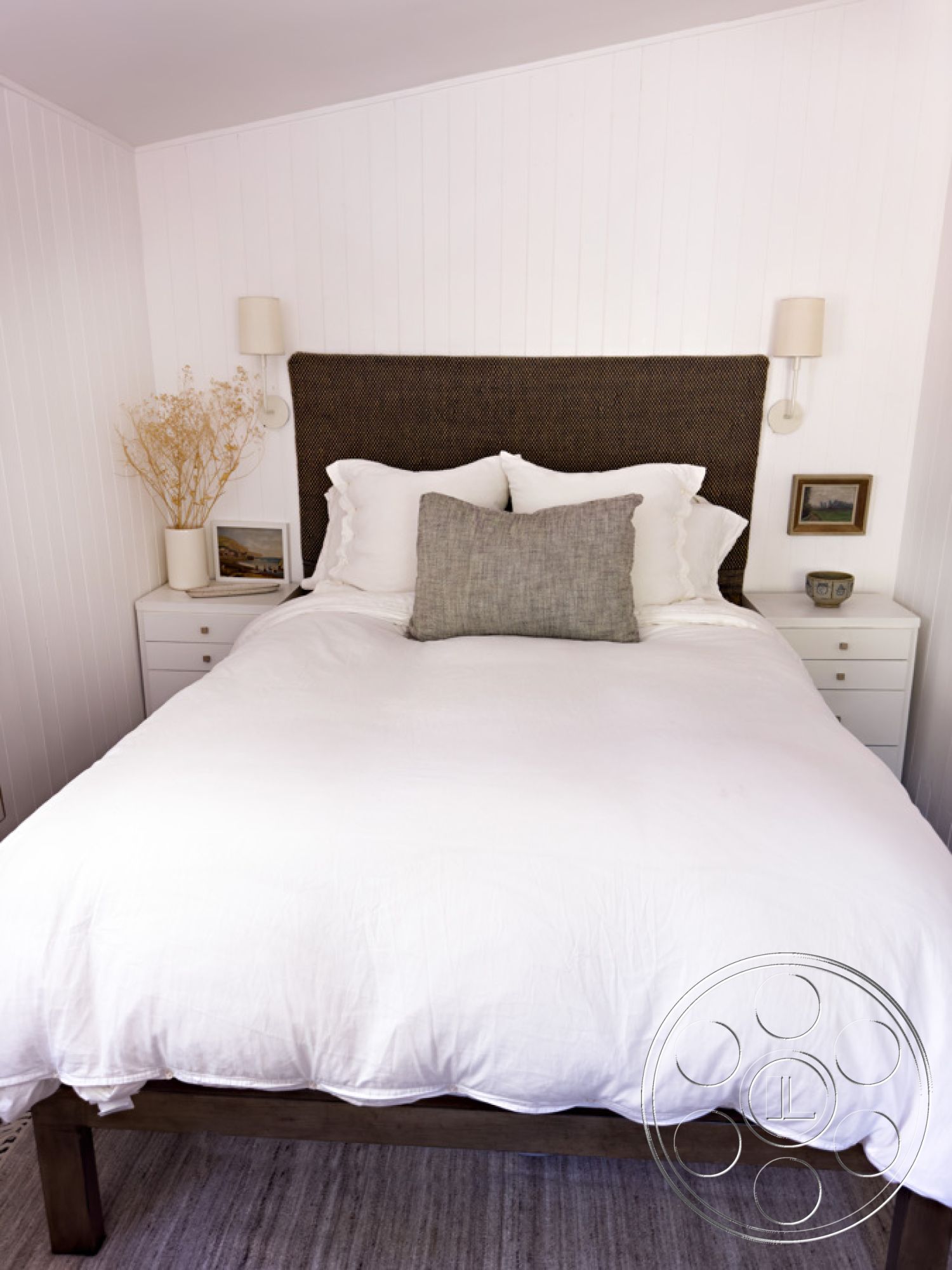 Ranch 33 - contemporary design elements, textured throw pillow, calming color palette, cozy bedroom setting, natural light interior, hardwood bedroom floors, neutral bedding accents, white painted walls, modern wall sconces, woven fabric headboard, minimalist bedside tables, decorative photo frames, simple ceramic vase