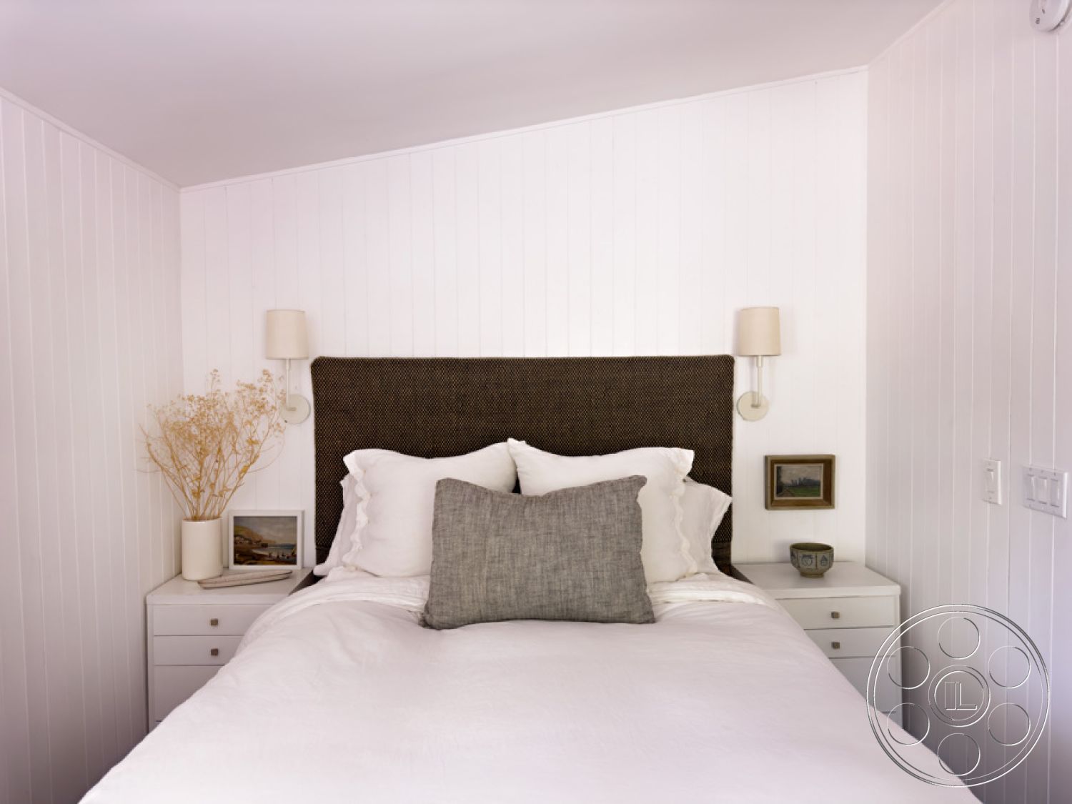 Ranch 33 - modern bedroom design, shiplap walls interior, textured white paneling interior, textured duvet cover bed, woven headboard bed, soft gray throw pillow bed, nightstand with ceramic lamp, minimalist bedside decor, brushstroke painting wall art, dried floral arrangement decor, bedroom lighting sconces, plaid accent pillow bed, luxurious bedding set, subtle coastal theme interior, neutral color palette bedroom, urban cozy bedroom