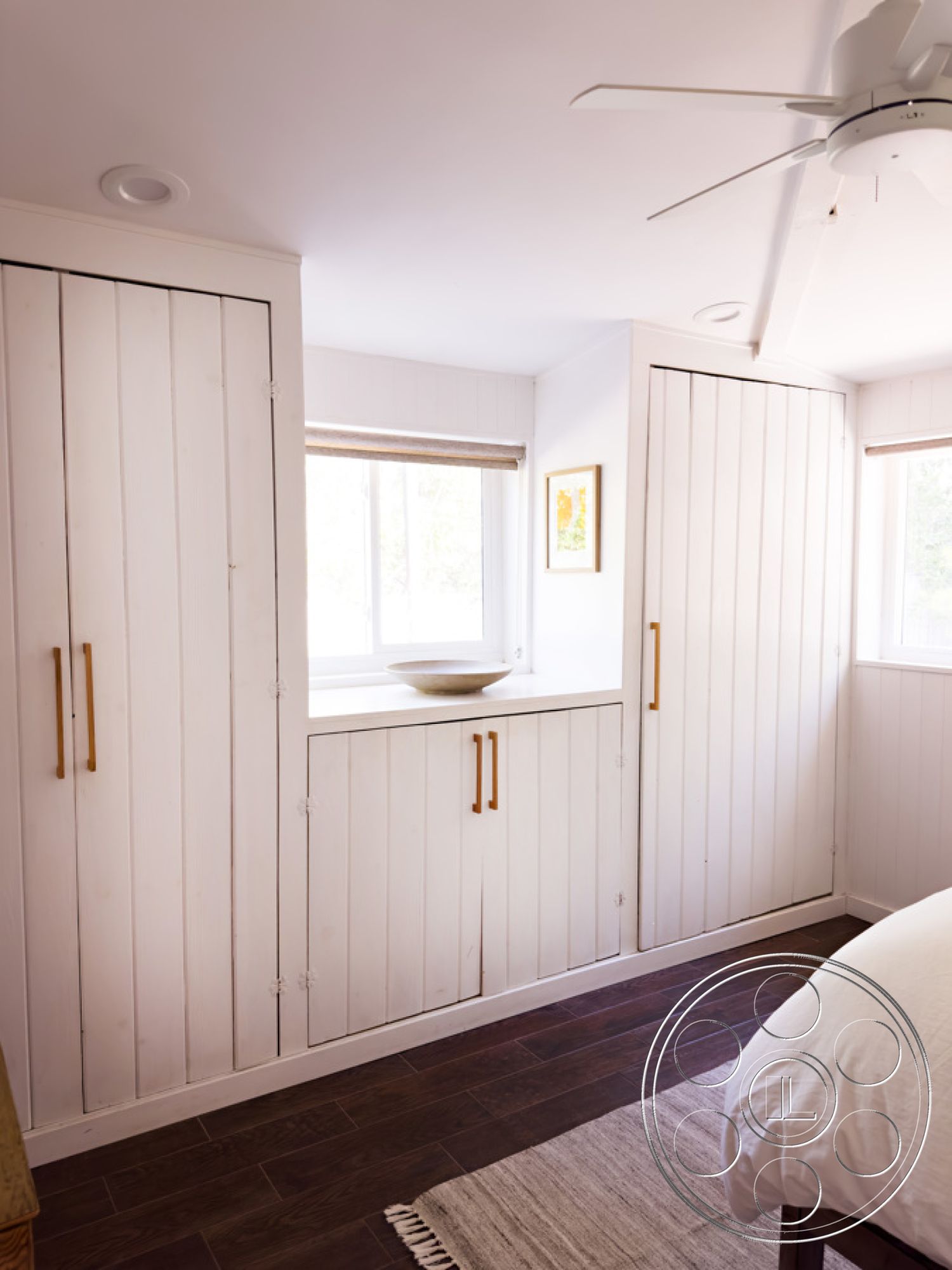 Ranch 33 - minimalist decor, neutral color palette, textured area rug, natural light from windows, cozy reading nook, modern ceiling fan, contemporary interior design, large window with natural light, functional storage solutions, white shiplap interior walls, dark hardwood bedroom flooring, built-in storage cabinets with gold hardware