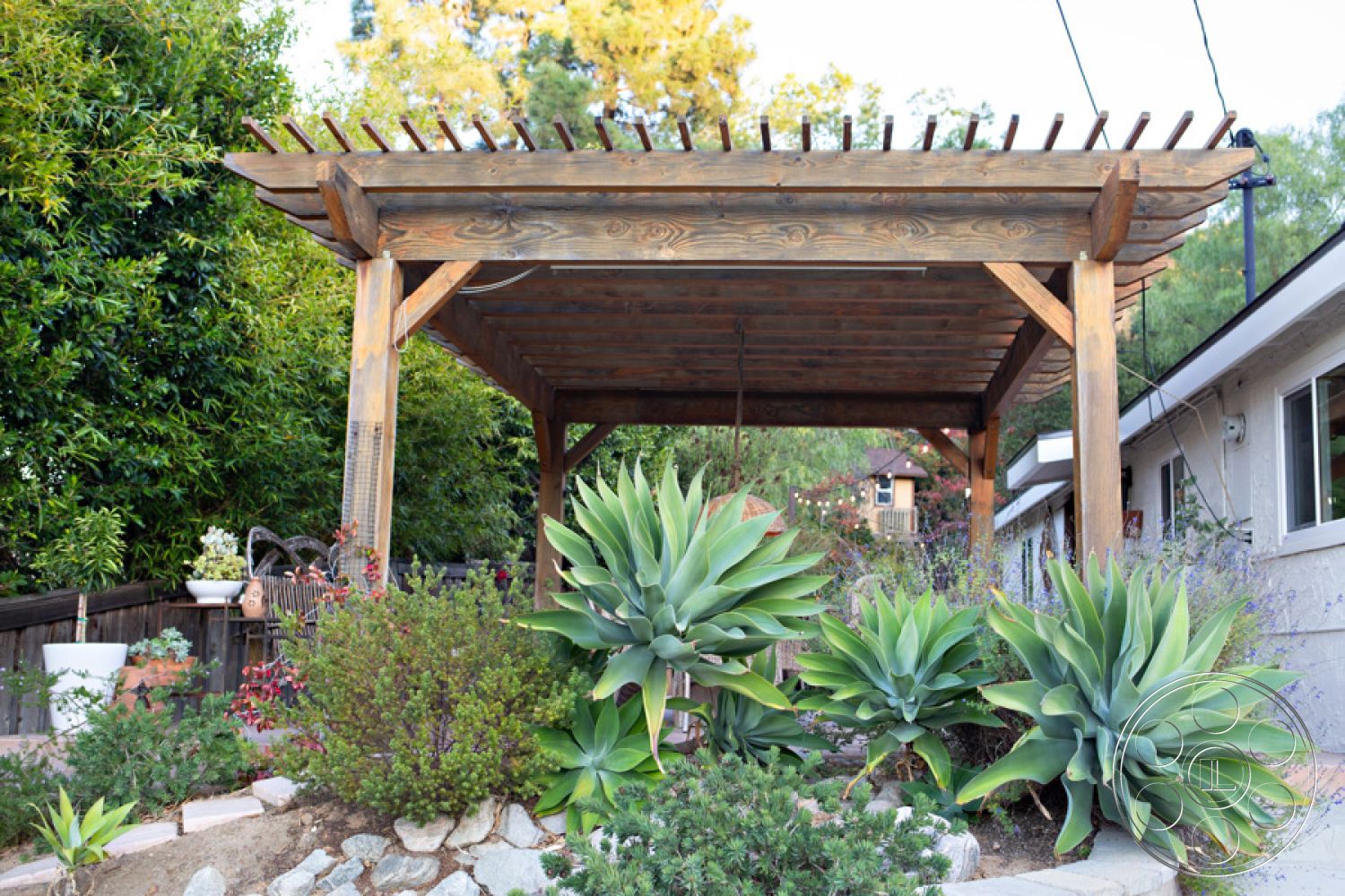 Ranch 33 - flowering bushes, natural greenery, exposed wood beams, outdoor living space, relaxation spot, suburban backyard, landscaped garden area, wood pergola structure, stone garden path, contemporary home exterior, succulent plant arrangements, patio setting, decorative garden pots, sun-dappled outdoor area, open air shelter, garden design elements