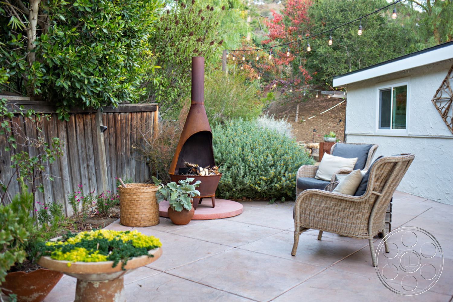 Ranch 33 - decorative stone planter, concrete patio flooring, exterior patio area, wooden deck railing, textured wood fence, wicker outdoor seating, rustic metal fireplace, landscaped garden with greenery, outdoor ambient lighting, tropical plants setting, natural hillside view