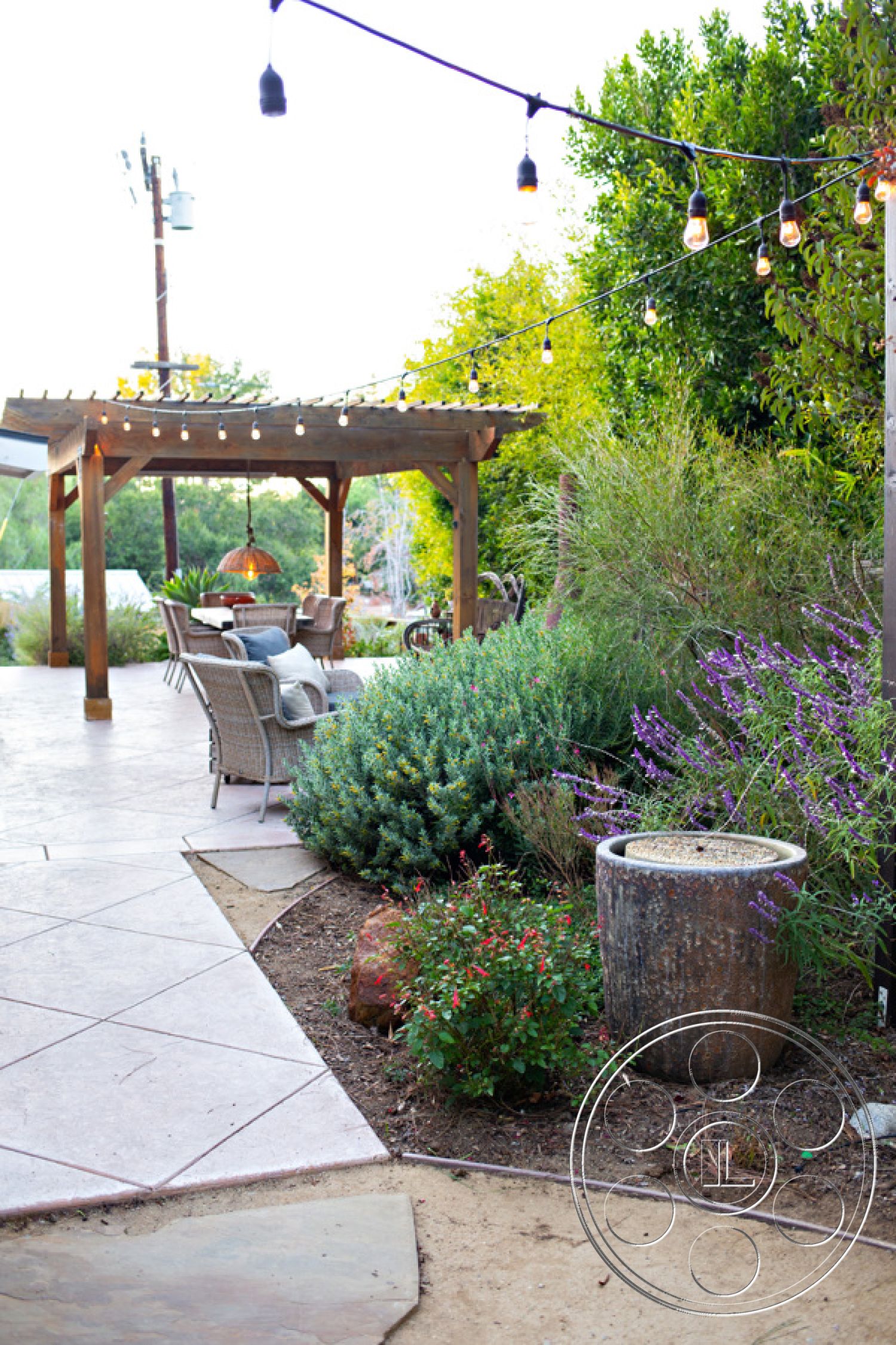 Ranch 33 - modern outdoor furniture, colorful flowering plants, outdoor dining space, textured concrete surface, decorative stone planter, curved garden path, wood pergola structure, landscaped garden beds, exterior patio area, low maintenance shrubs, stamped concrete patio flooring, string light fixtures, seasonal outdoor lighting