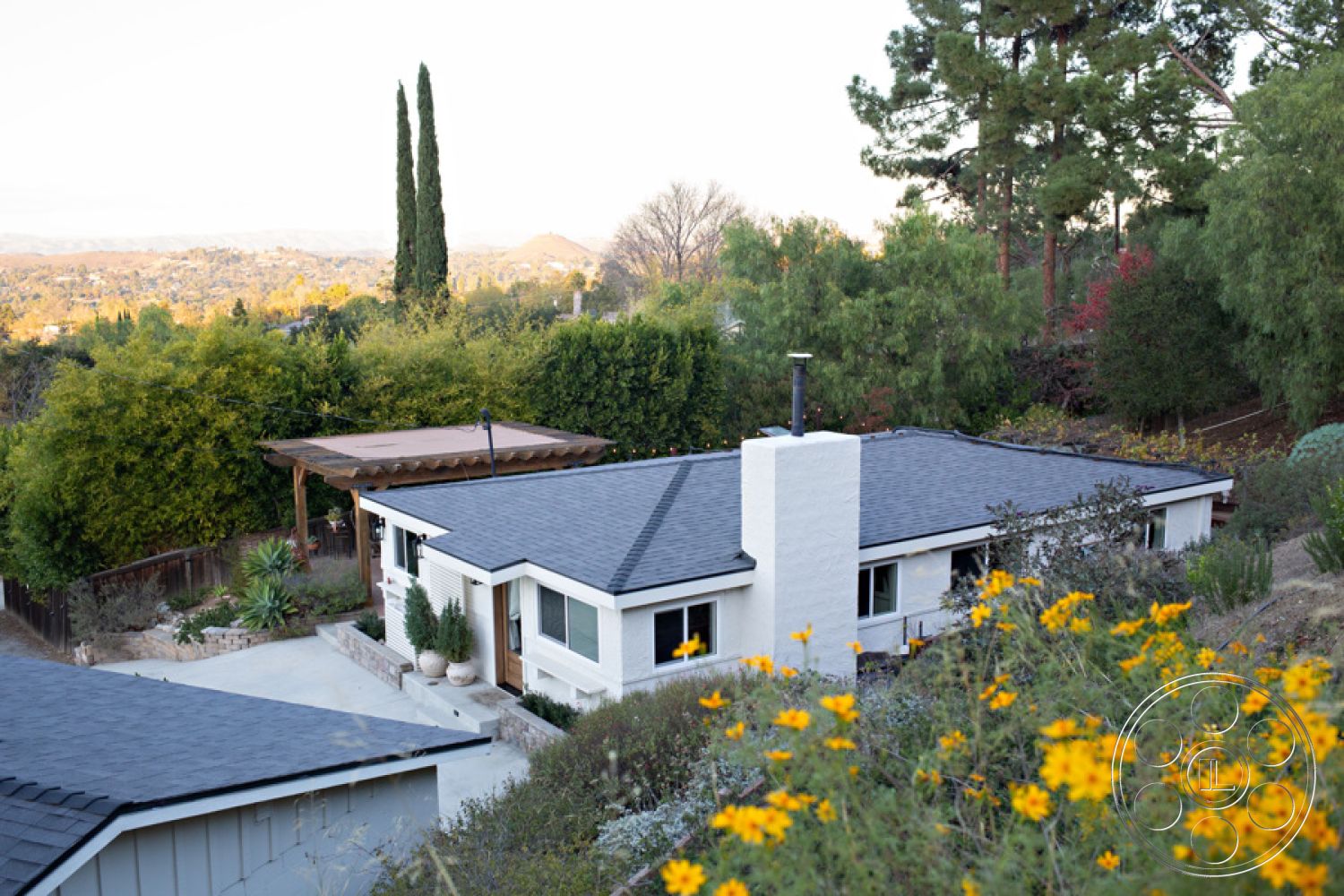 Ranch 33 - exterior - flat roof design, exterior - stone garden retaining wall, exterior - white stucco siding, exterior - dark shingle roof, exterior - wooden pergola over patio, exterior - concrete driveway with gravel finish, exterior - landscaped garden with wildflowers, exterior - horizontal wood slat fencing, exterior - paved outdoor seating area, configuration - single-story home, setting - hillside location with valley view, setting - surrounded by lush greenery, architectural style - Mid-Century Modern, room function - outdoor relaxation space