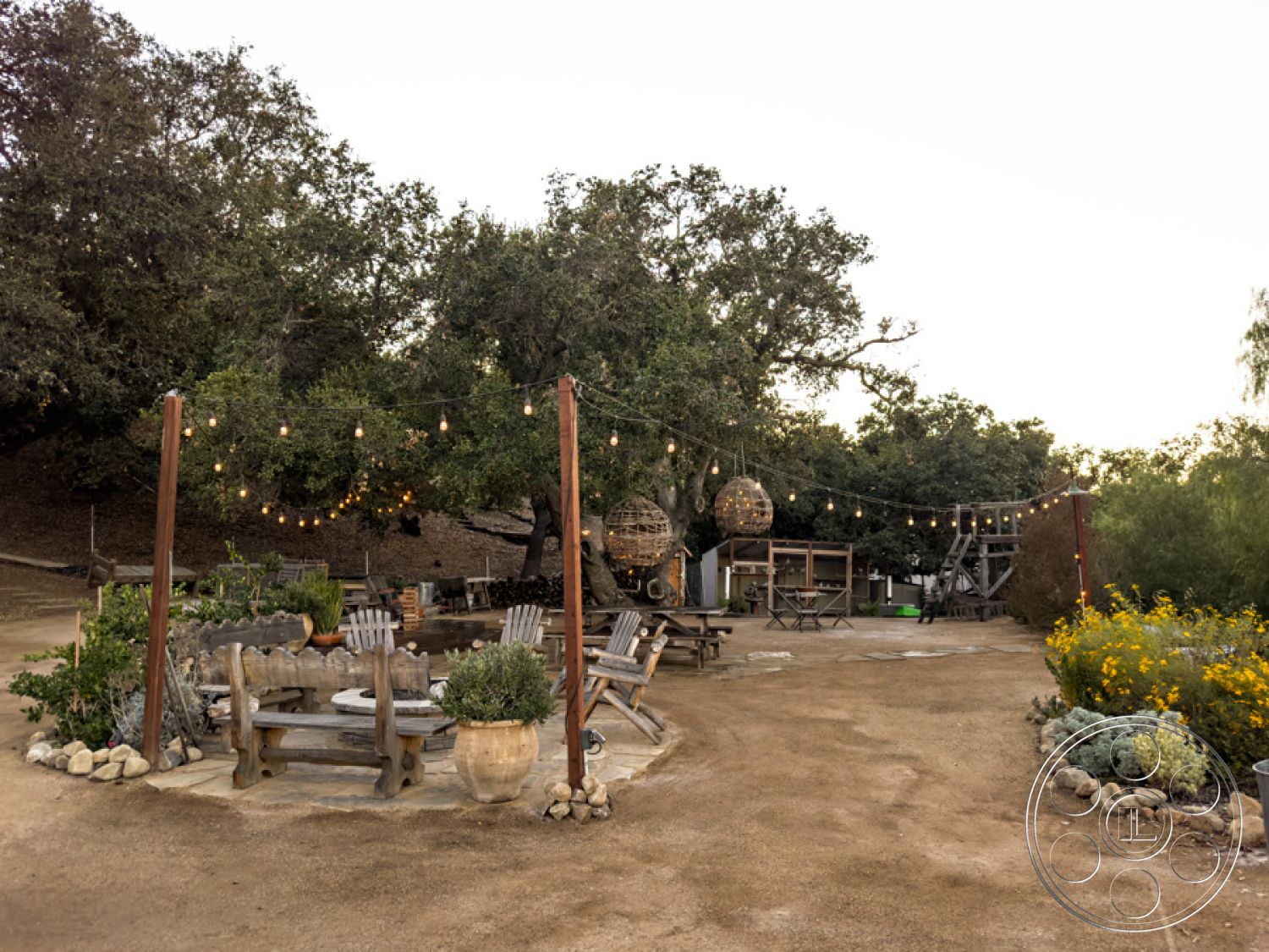 Ranch 33 - earthy color palette, barbecue area, exposed wood beams, twinkling string lights, gravel landscaping, wooden adirondack chairs, landscaped garden beds, dense tree canopy, open outdoor seating area, natural stone patio flooring, organic garden design, casual outdoor lounge, woven hanging light fixtures, rustic wooden outdoor table, decorative garden planters, etched stone fire pit, vibrant wildflower garden, relaxed rural setting, cozy outdoor gathering spot, spacious dirt pathway, seasonal outdoor decor, rustic farmhouse charm, sunset backyard view, family-friendly outdoor space