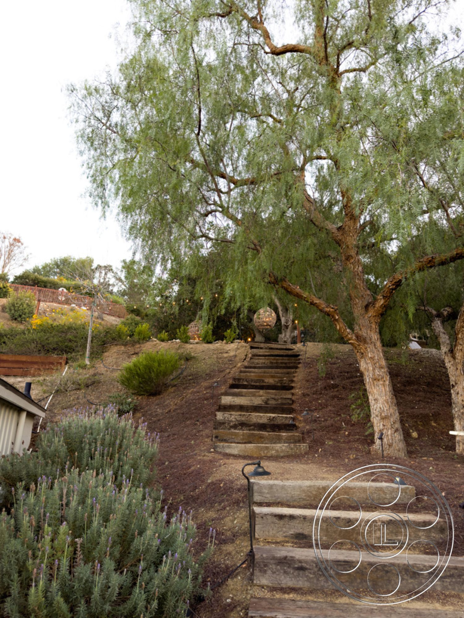 Ranch 33 - outdoor lighting fixtures, lush green trees, landscaped garden area, exterior natural stone accents, rustic garden design, serene outdoor environment, native plant landscaping, outdoor pathway lighting, wooden stepping stones, natural hillside steps, lavender plant borders, gentle sloping terrain, sustainable garden setting, hardscape pathway materials, Mediterranean-inspired garden