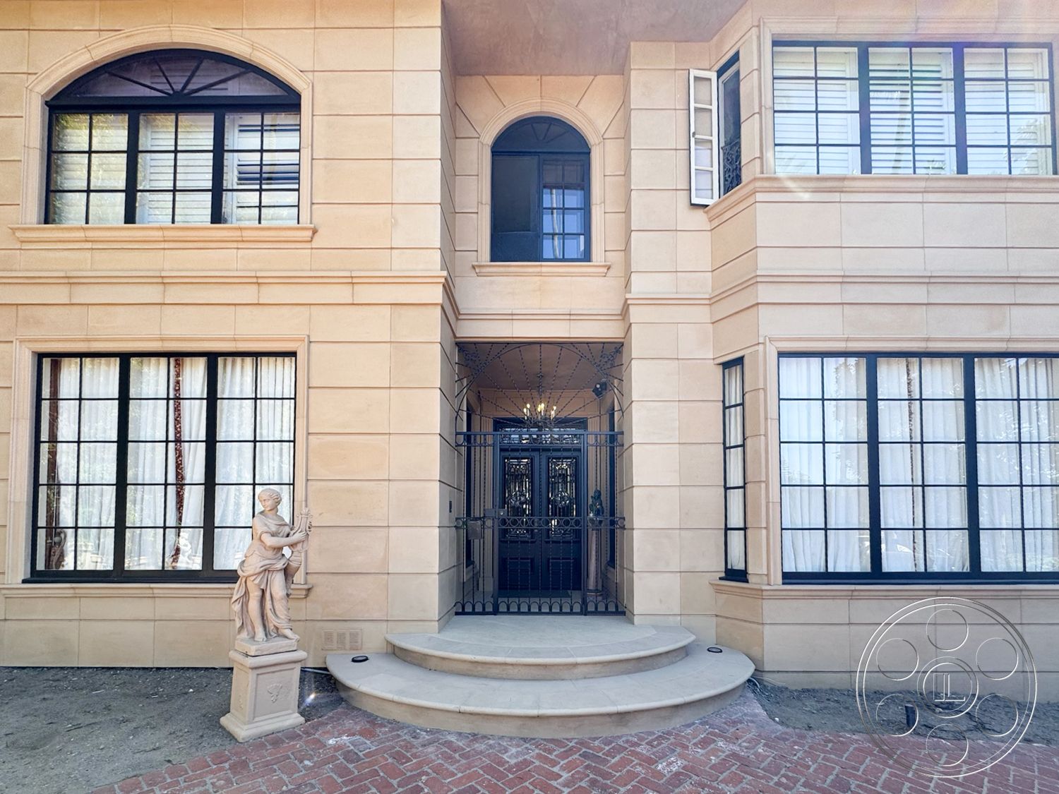 Mansion 146 - exterior, transom windows, symmetrical facade, arched doorways, decorative moldings, classic architectural details, double-hung windows, traditional home design, brick paver driveway, sandstone facade, black metal security gate, elegant front steps, stone statue, setback landscaping