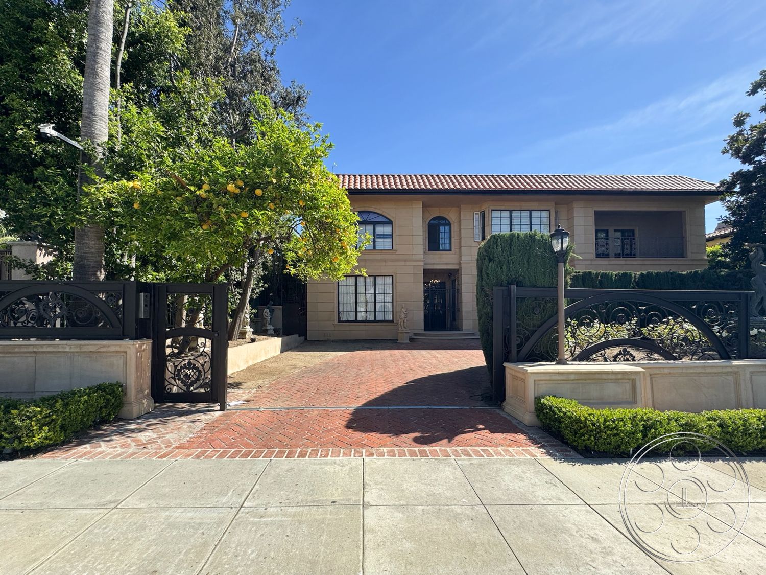 Mansion 146 - exterior, warm color palette, symmetrical facade, red tile roof, cobblestone walkway, wrought iron gate, stucco exterior walls, decorative stone accents, brick driveway pavers, two-story residence, transom windows above doors, landscaped garden with hedges, tropical garden setting, built-in outdoor lighting, arched front windows, lemon tree in garden, palm trees in front yard, residential entrance pathway, home with courtyard, grand front entrance