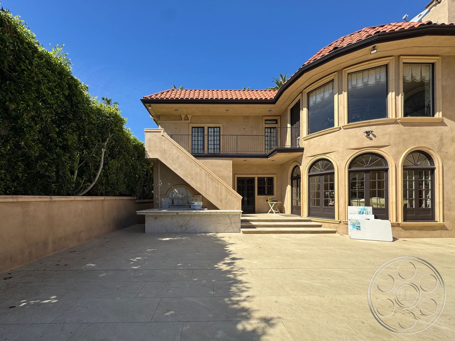 Mansion 146 - large glass doors, red tile roof, scenic outdoor space, arched windows, Mediterranean architectural style, elegant terrace, two-story home, open-air layout, concrete patio flooring, exterior stucco walls, sunny outdoor environment, courtyard setting, staircase with concrete steps, balcony with metal railings, outdoor kitchen with built-in grill, landscaped green hedges, decorative window trims, dining terrace adjacent to the house