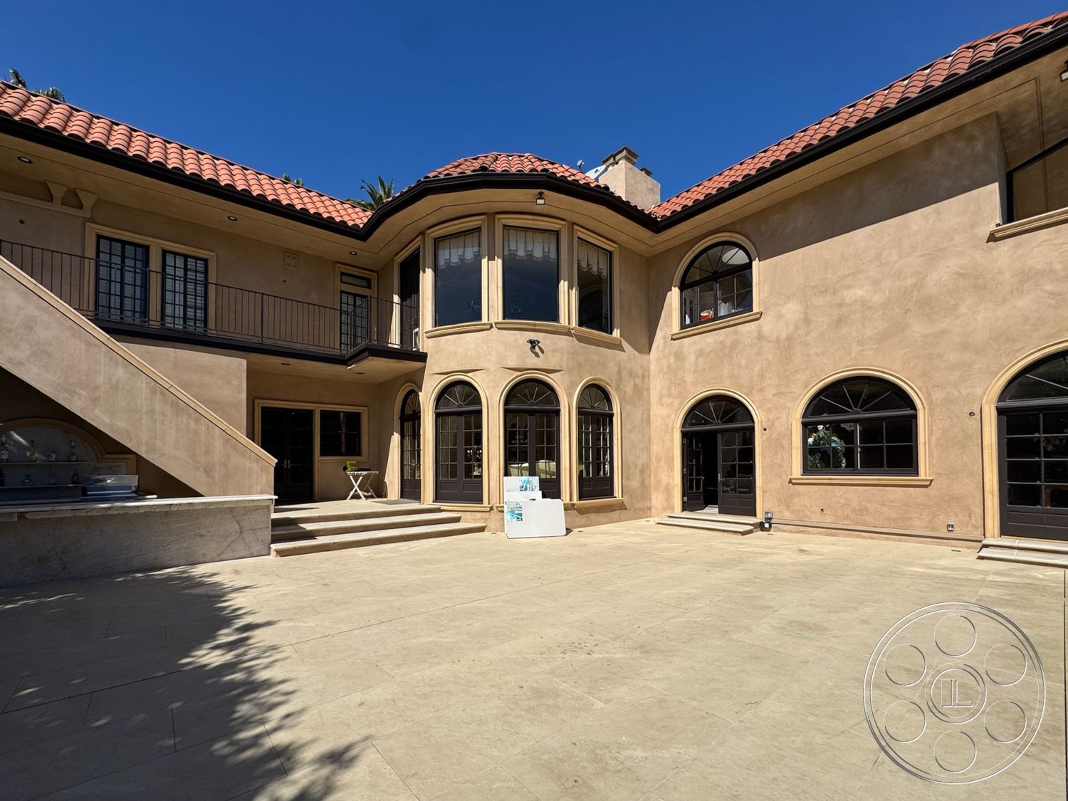 Mansion 146 - outdoor living space, black framed windows, terracotta tile roof, arched windows, elevated terrace, traditional architectural style, balcony with wrought iron railings, two-story home, concrete patio flooring, stucco exterior walls, palm tree landscaping, courtyard setting, vaulted ceiling details, patio area for relaxation, sunny exterior environment, exposed step details