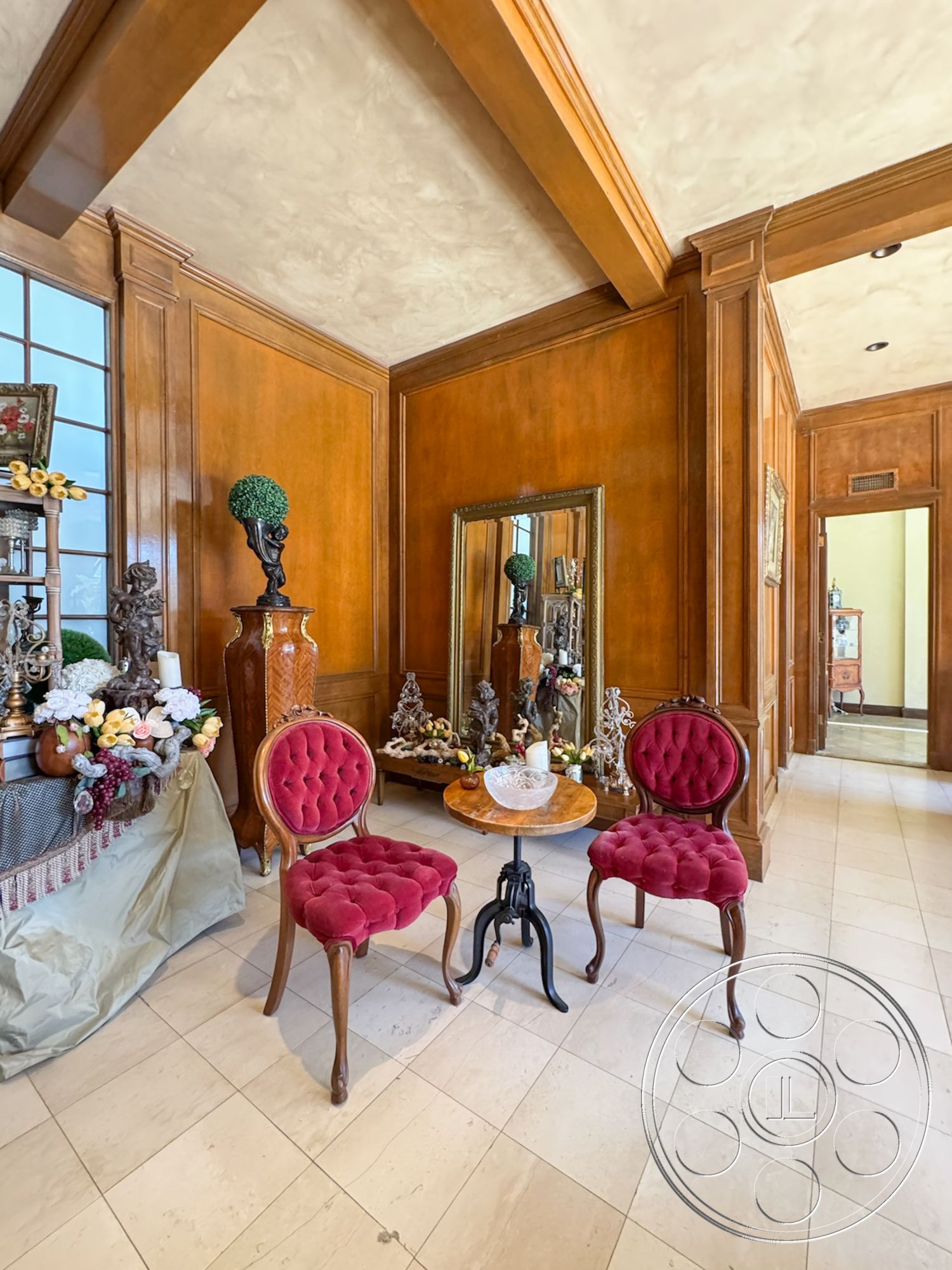 Mansion 146 - textured plaster ceiling, natural light from windows, round wooden side table, traditional interior design, exposed wood paneling, symmetrical room layout, red velvet tufted chairs, marble-like tile flooring, ornate decorative sculptures, framed mirror with ornate details, decorative floral accents, dimensional wood beam ceiling, luxurious interior hallway, classic antique furnishings