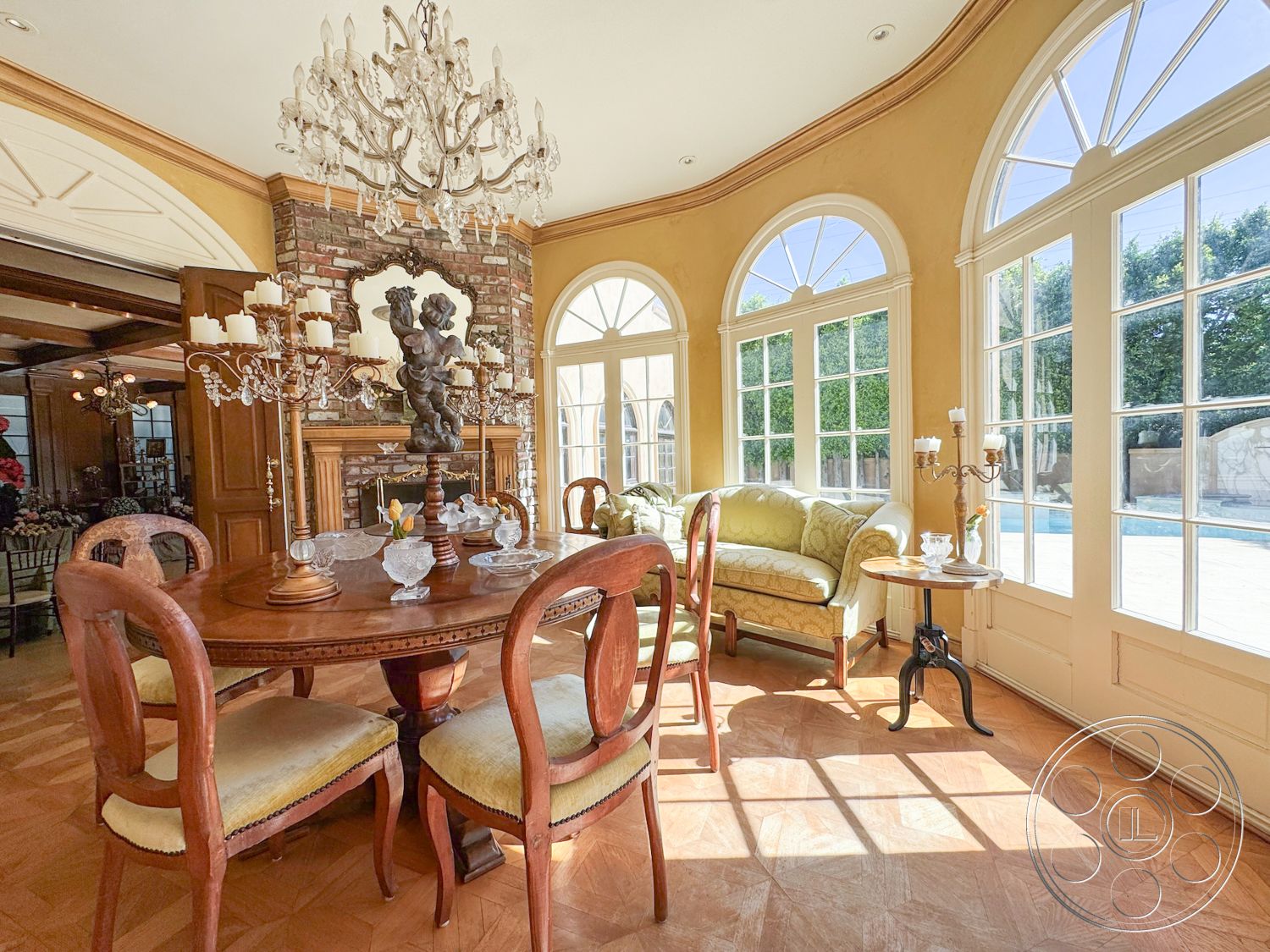 Mansion 146 - crystal chandelier, large arched windows, interior dining area, exposed brick fireplace surround, neutral painted walls, parquet hardwood flooring, cozy and inviting atmosphere, natural light flooding the room, wooden dining table with ornate detail, classic wooden chair with yellow upholstery, plush green upholstered sofa, decorative wooden moldings, traditional candelabra, antique glassware on table, intricate ceiling details, elegant dining setting, lush outdoor view through windows, formal dining room