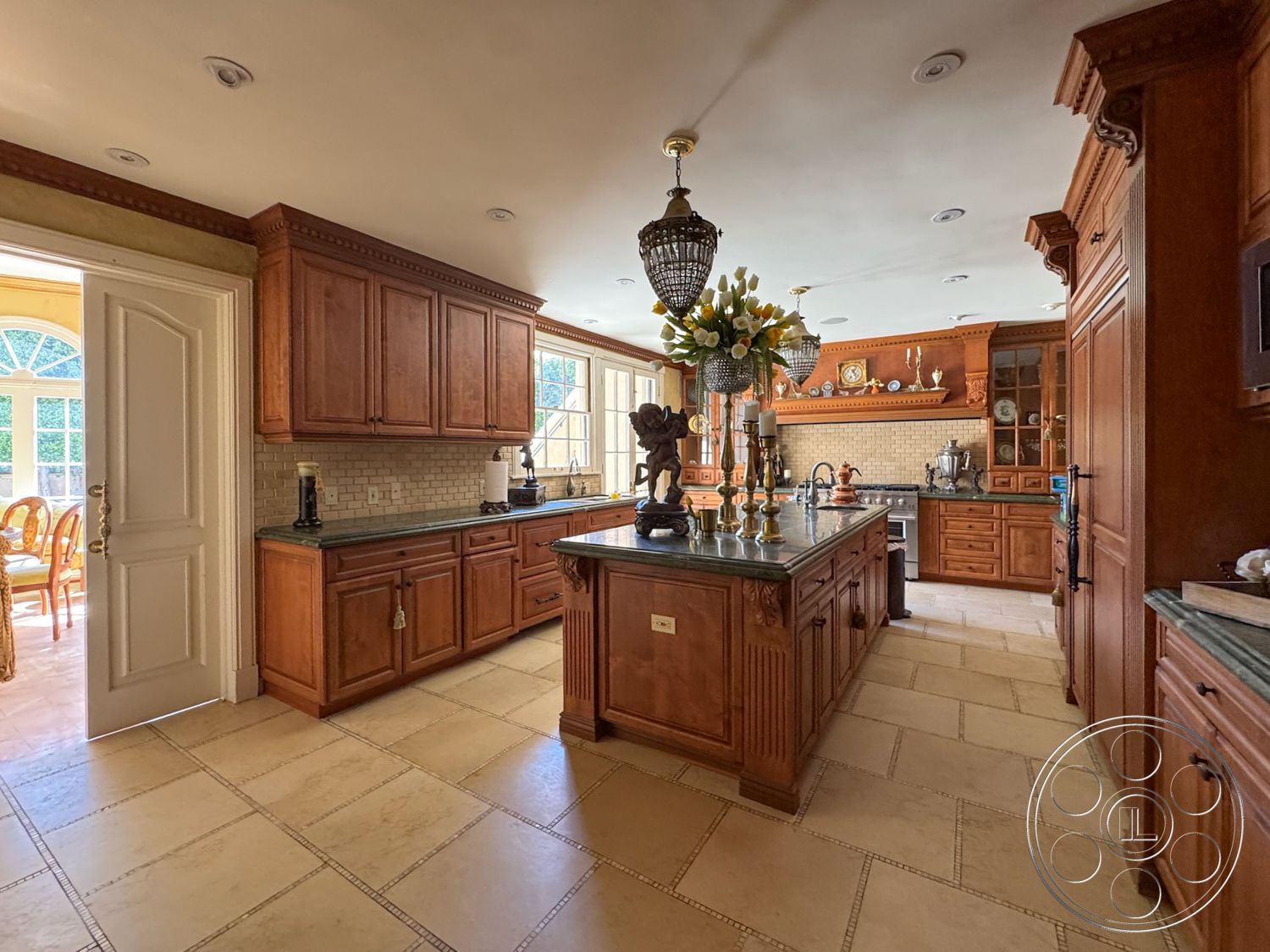 Mansion 146 - neutral color palette, open floor plan, decorative crown molding, exposed light fixtures, textured tile flooring, traditional architectural style, interior kitchen, elegant pendant lighting, granite kitchen countertops, island kitchen design, large bay windows, brass faucet fixtures, custom wood cabinetry, tumbled stone backsplash