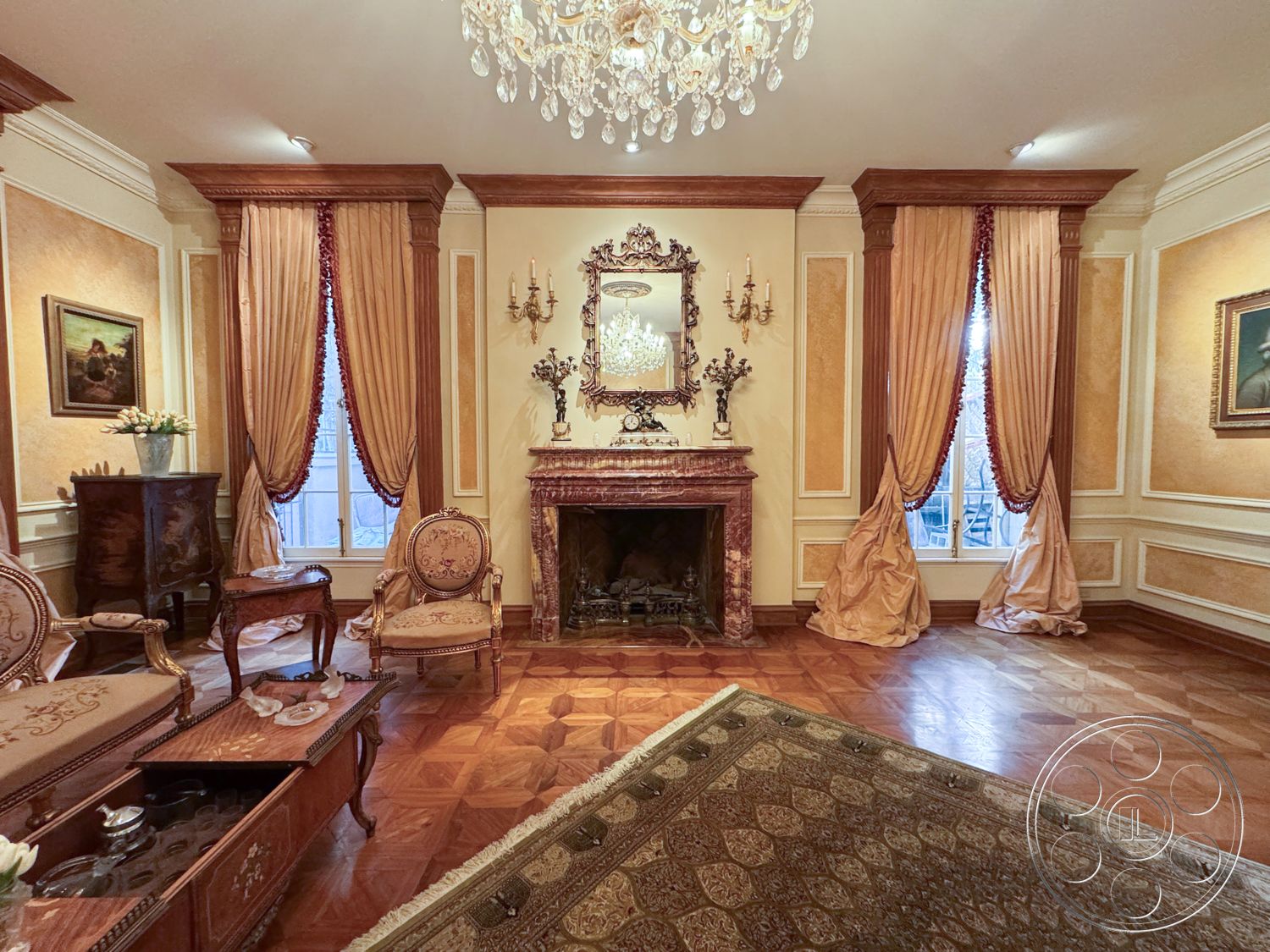 Mansion 146 - dark wood furniture, historic architectural details, marble fireplace surround, herringbone hardwood living room floors, exposed wood crown molding, ornate crystal chandelier, decorative wall sconce lighting, luxurious sitting area, intricate area rug, white painted walls with gold accents, velvet drapes with tassel trim, classic portrait artwork, elegant vintage seating, traditional European design elements