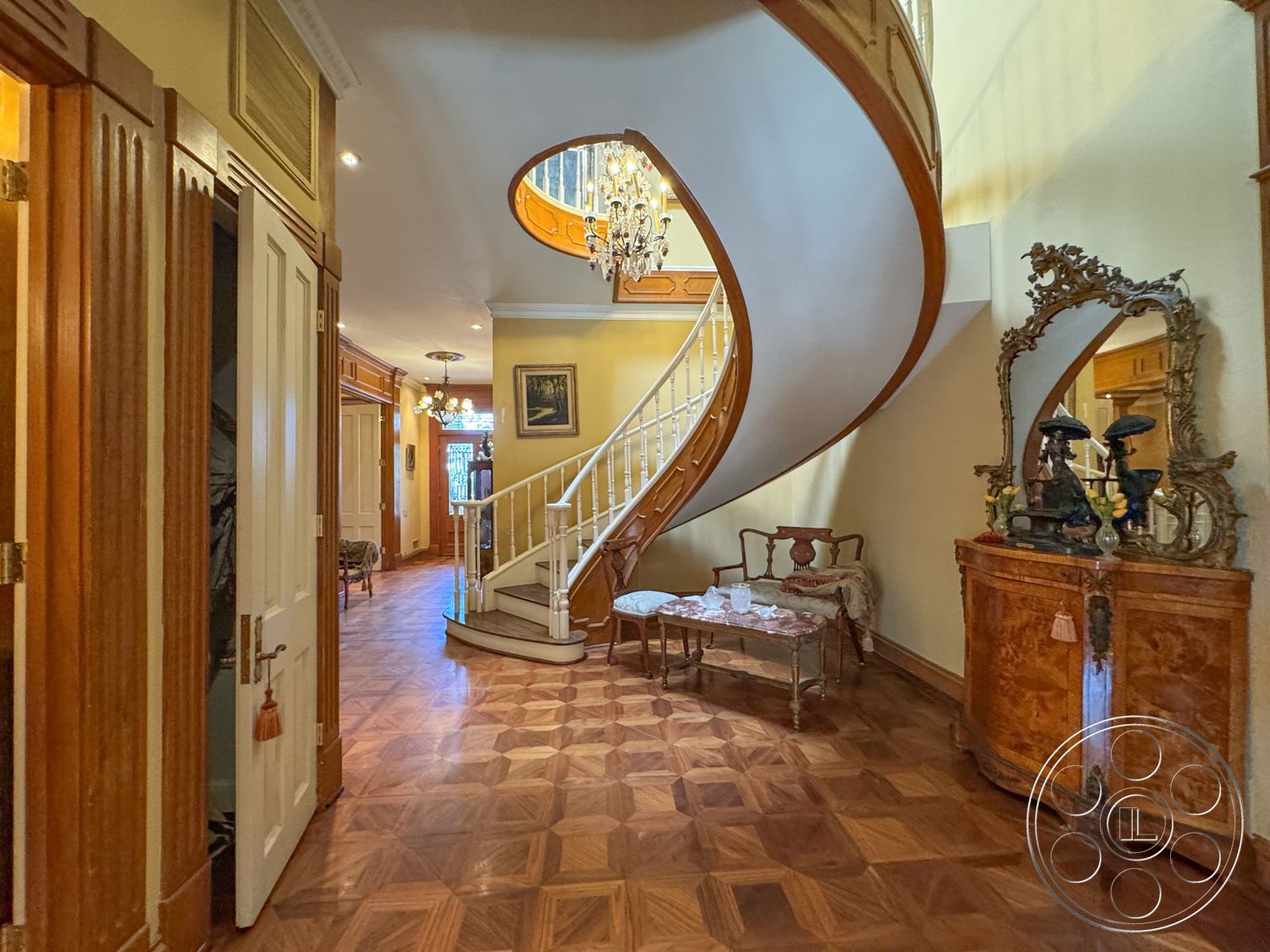 Mansion 146 - neutral wall colors, decorative mirror, chandelier lighting, double doors, decorative accents, framed wall art, elegant entryway, antique furniture, curved staircase, spacious hallway, historic architectural details, open foyer, classic interior design, ornate wall moldings, natural light from upper windows, parquet floor pattern, wooden staircase railing, intricate hardwood flooring, trimmed door casings, ceilings with crown molding