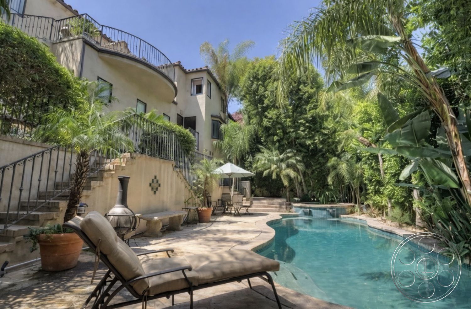 Medit 167 - floor-to-ceiling windows, stone pool deck, private pool area, oval swimming pool, wrought iron railings, exterior concrete patio floor, lush green foliage, stucco house exterior, sunlit outdoor space, landscaped tropical garden, curved patio layout, concrete steps with stone edging, outdoor lounge area with sun loungers, backyard palm tree setting, terraced garden with potted plants, sandy beige stone pavers, canopy umbrella for outdoor shading, natural stone wall features, architectural Mediterranean style