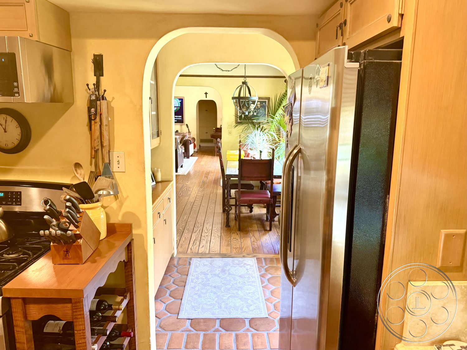 Medit 167 - neutral color palette with warm tones, interior kitchen with stainless steel appliances, textured plaster wall finishes, functional kitchen layout with ample storage, tile kitchen floor with terracotta design, arched doorway leading to dining area, oak hardwood living room flooring, built-in wooden kitchen cabinets, open-concept design with visible dining area, decorative chandelier hanging in dining room, kitchen island with wooden countertop, pantry space adjacent to kitchen area, plant accents visible in dining area