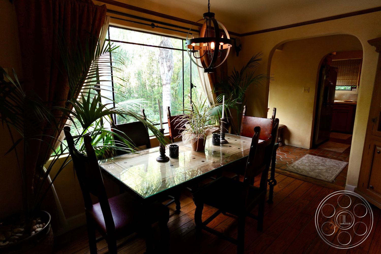 Medit 167 - neutral color palette, natural light from large windows, textured plaster walls, decorative pendant lighting, wooden dining chairs, interior dining room, hardwood dining room floors, greenery indoor plants, soft fabric curtains, arched entryway to kitchen, glass tabletop dining table, rustic dining decor, brick flooring in adjacent kitchen