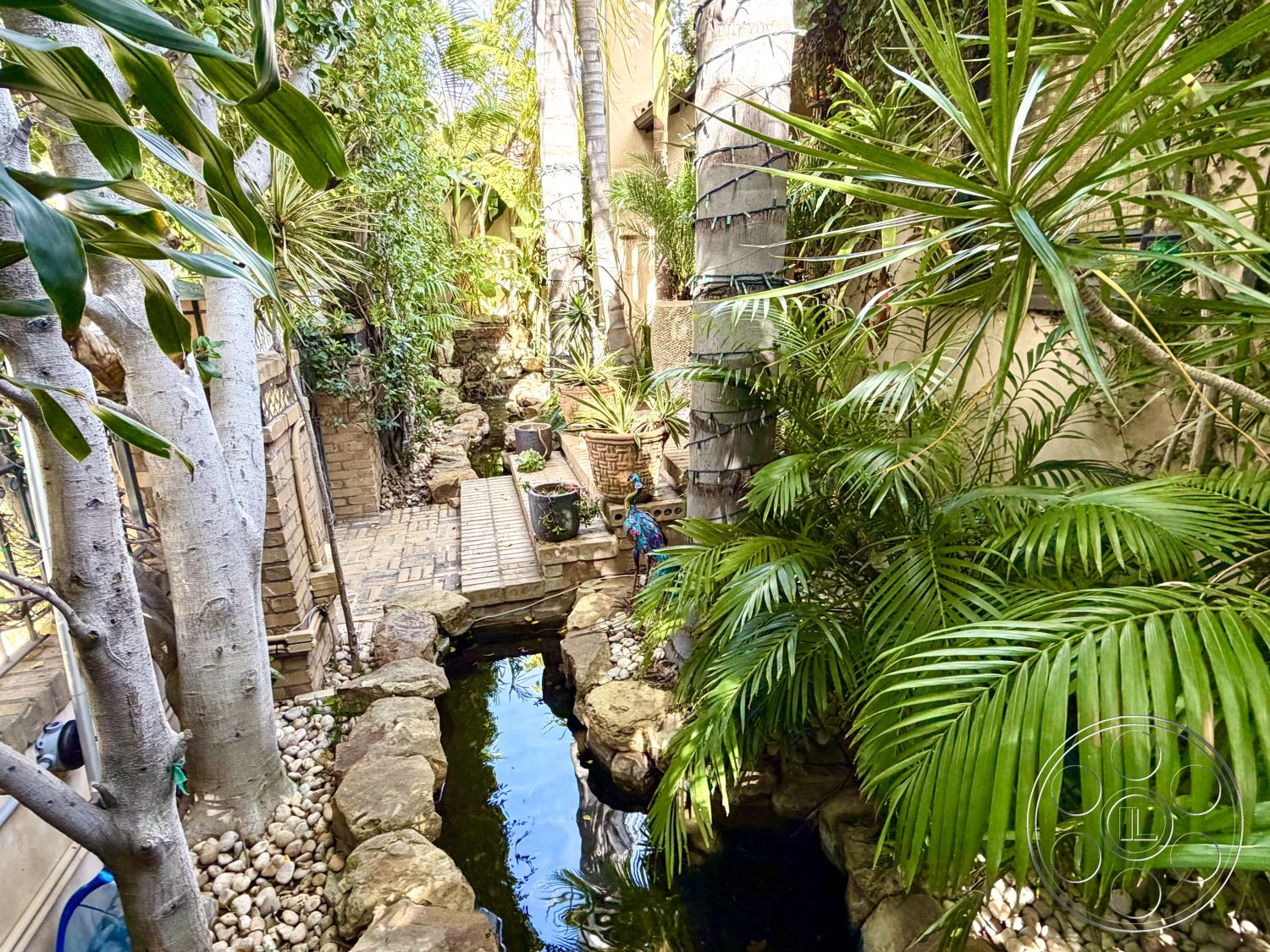 Medit 167 - lush greenery landscaping, textured stone border, interior garden setting, brick garden pathway, pebbled riverbed landscape, stacked stone water feature, tropical palm planting, wooden bridge over water, woven planter baskets, exposed root system of trees, natural pond with aquatic plants, curved path layout, bamboo garden accents, secluded oasis style, organic flowing forms, custom outdoor lighting fixtures, vertical garden walls, peaceful relaxation area