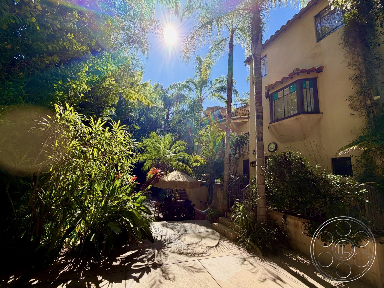 Medit 167 - arched windows, wooden patio furniture, natural stone steps, Mediterranean architectural style, textured stucco walls, proximity to greenery, concrete patio flooring, urban outdoor retreat, palm trees landscaping, exterior courtyard space, tropical garden setting, thatched roof umbrella, cast iron railings, multi-level outdoor area, Sunlit garden, vibrant plants and flowers