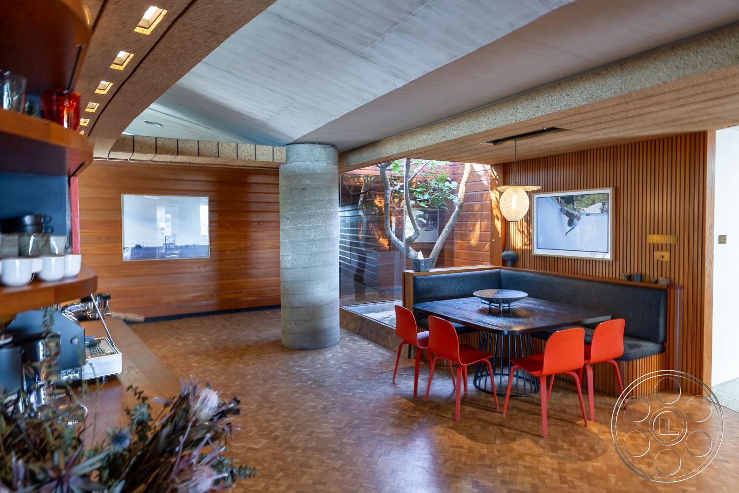 Silvertop House - neutral color palette, modern pendant lighting, round dining table, exposed concrete ceiling, mid-century modern style, curved wall, parquet flooring, open-plan living space, wood beam ceiling, wood panel accent wall, flush baseboards, flat roof architecture, interior living area, glass wall with garden view, high-ceiling interior, polished concrete column, built-in dining nook, red plastic dining chairs, kitchen shelf with utensils, natural light from glass wall