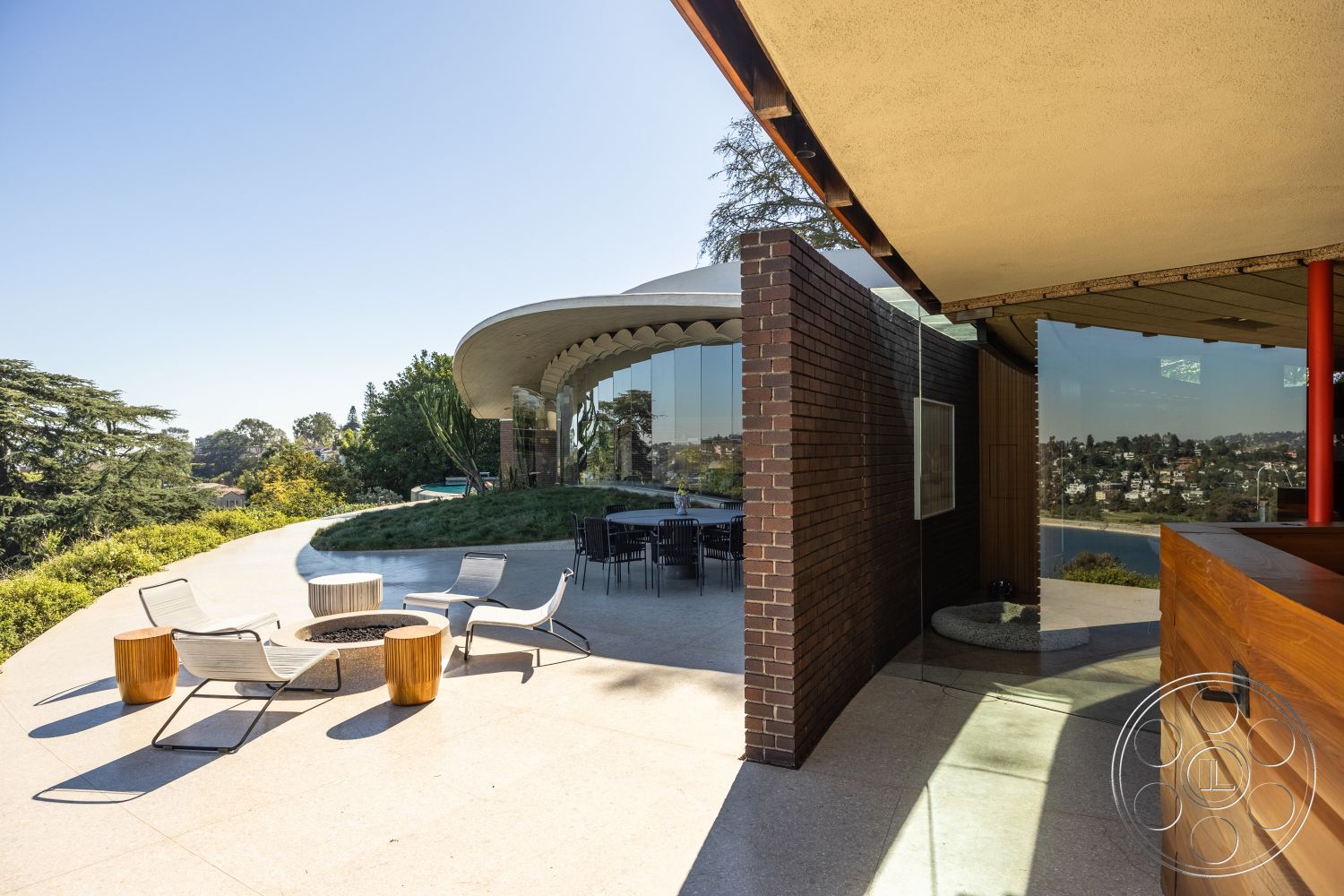 Silvertop House - natural light, exterior, landscaped garden, open floor plan, surrounding trees, smooth concrete flooring, brick accent wall, modern architectural style, hillside location, glass wall, wooden outdoor furniture, round fire pit, minimalist outdoor space, curved concrete patio, stainless steel outdoor dining set, sculptural roof design, broad views