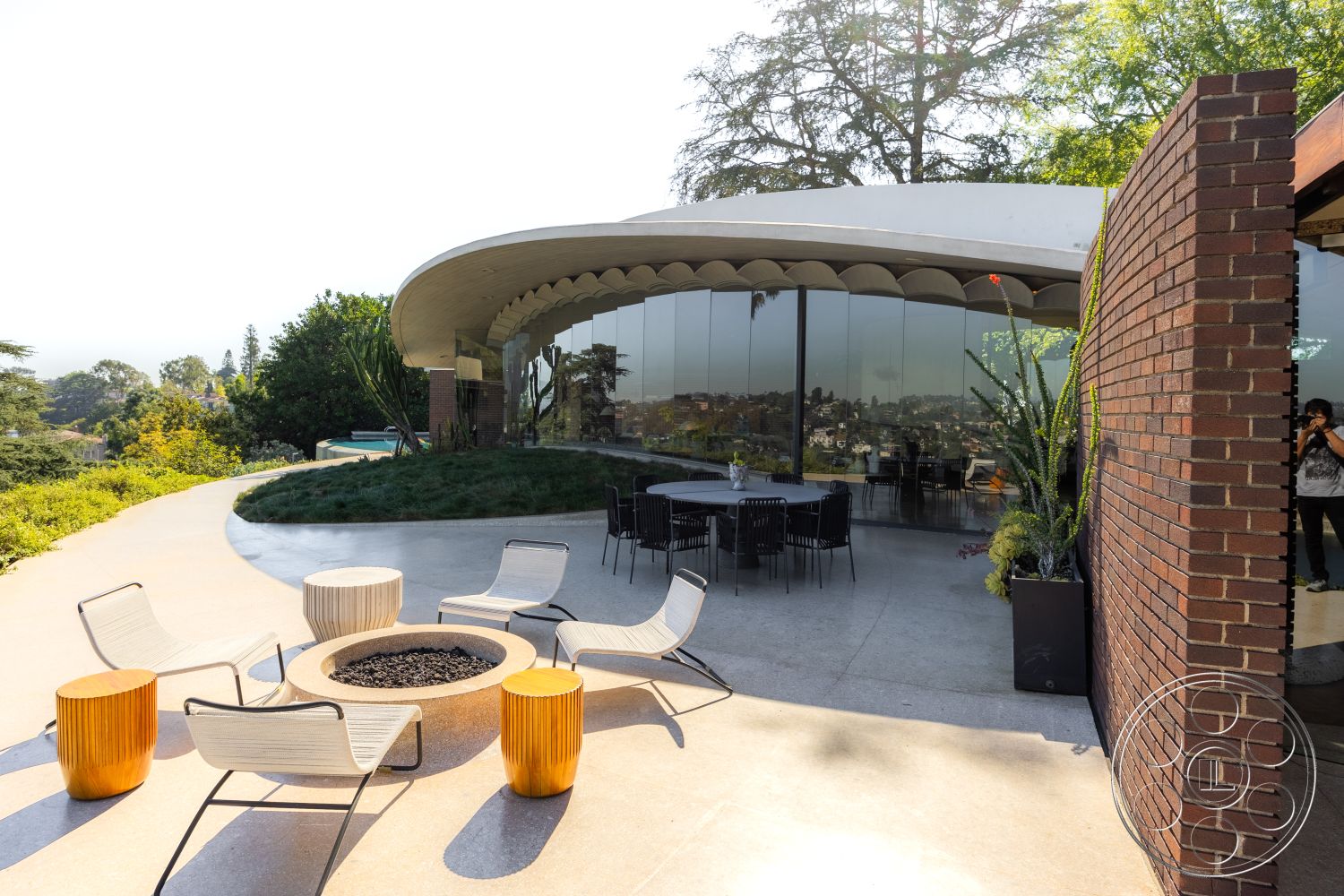 Silvertop House - smooth concrete surfaces, exterior concrete patio floor, floor-to-ceiling glass windows, natural greenery backdrop, exterior glass wall, landscape garden setting, exterior dining area, stylish lounge seating, curved patio shape, exterior brick feature wall, sleek modern outdoor chairs, contemporary round fire pit, luxury hillside view, exposed concrete deck, architectural mid-century modern style, urban retreat atmosphere, private outdoor gathering space