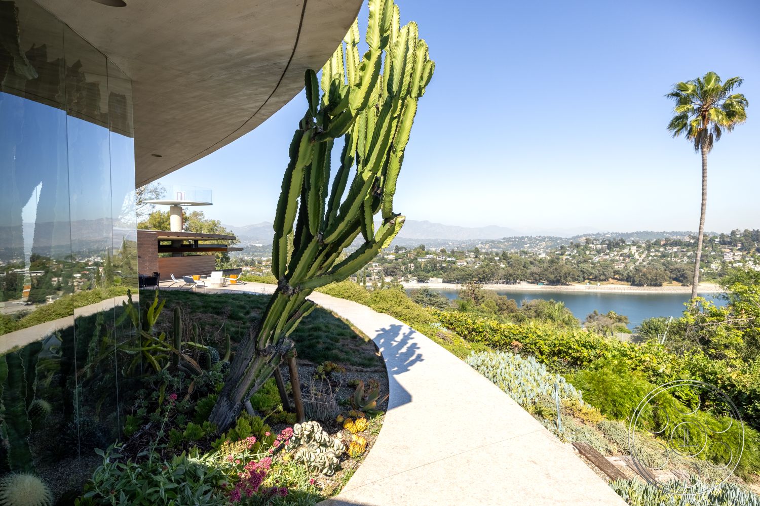 Silvertop House - open-air space, outdoor lounge area, sustainable landscaping, landscaped garden area, urban hillside location, concrete foundation, contemporary architectural design, natural light-filled spaces, modern hillside home, exterior glass walls, desert plants landscaping, infinity edge pool view, steel balcony railing, curved concrete patio walkway, panoramic city view setting, exposed natural stone elements