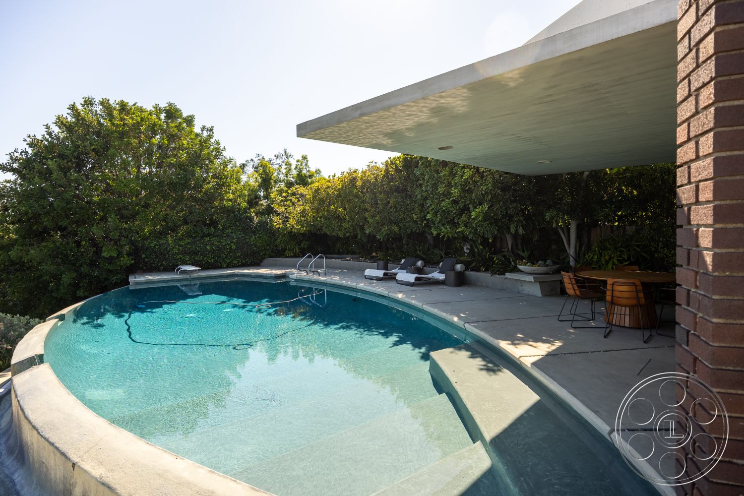 Silvertop House - glass sliding doors, water feature, outdoor entertaining space, concrete pool deck, rectangular pool, sun-drenched patio, landscaped garden area, concrete patio flooring, brick column details, private backyard oasis, modern outdoor living space, modern cantilevered roof, exterior concrete pool edge, poolside sun loungers, wooden outdoor dining set, green shrubbery backdrop, curvilinear pool shape, concrete lounge area, skylights for natural light