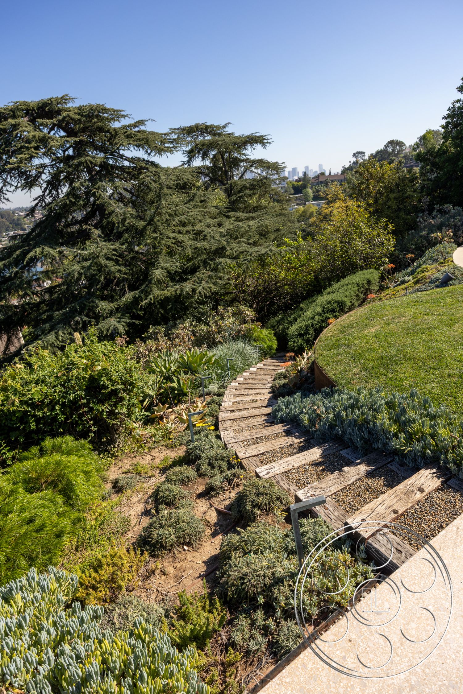 Silvertop House - outdoor living space, lush green lawn, urban skyline view, textured foliage, curved garden path, exterior garden setting, sustainable landscape design, wooden stepping stone pathway, rounded gravel path, native drought-resistant landscaping, elevated backyard garden, flexible stone border, walking trail through foliage, natural habitat integration, vertical plant arrangements