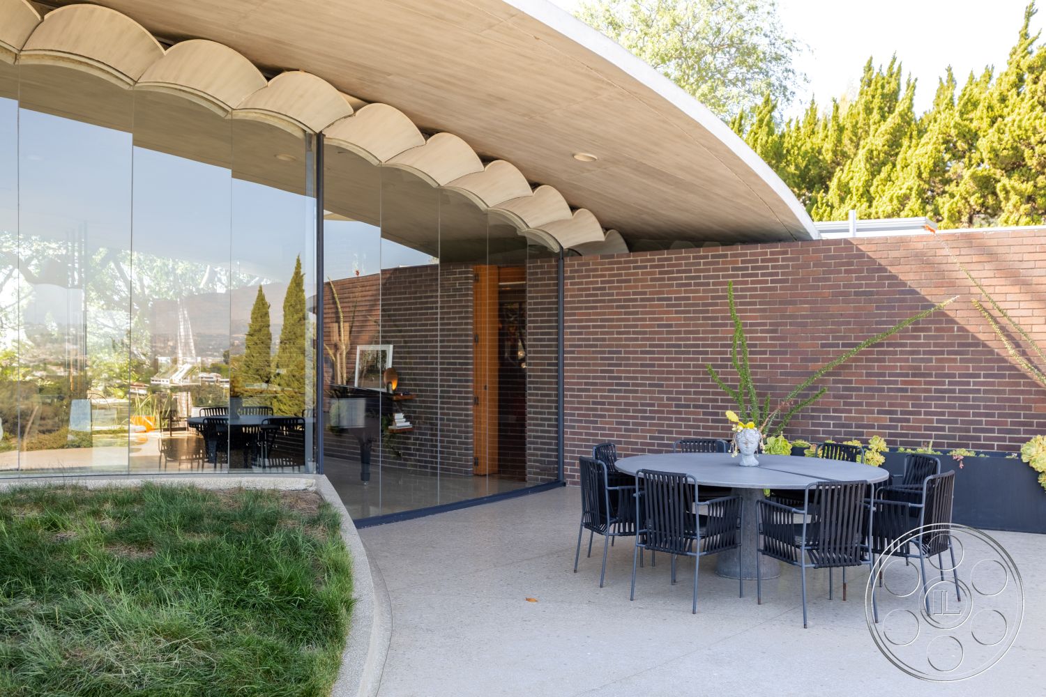 Silvertop House - exterior, contemporary architecture, wooden ceiling beams, seamless indoor-outdoor flow, minimalist patio furniture, modern outdoor dining area, glass curtain wall, urban hillside setting, textured concrete patio flooring, brick wall façade, curved concrete overhang, landscaped grass area, sculptural outdoor lighting, integrated plant bedding, varied ceiling heights