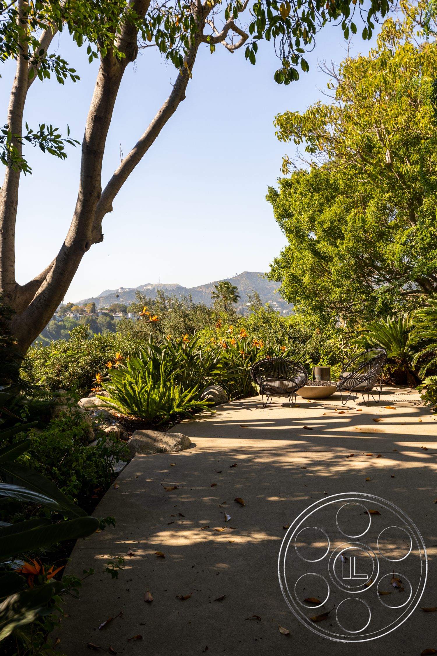Silvertop House - outdoor seating area, tropical plants, mountain view, circular concrete table, sunny exterior, concrete patio flooring, landscaped garden setting, leafy tree canopy, decorative stone borders, mid-century modern chairs
