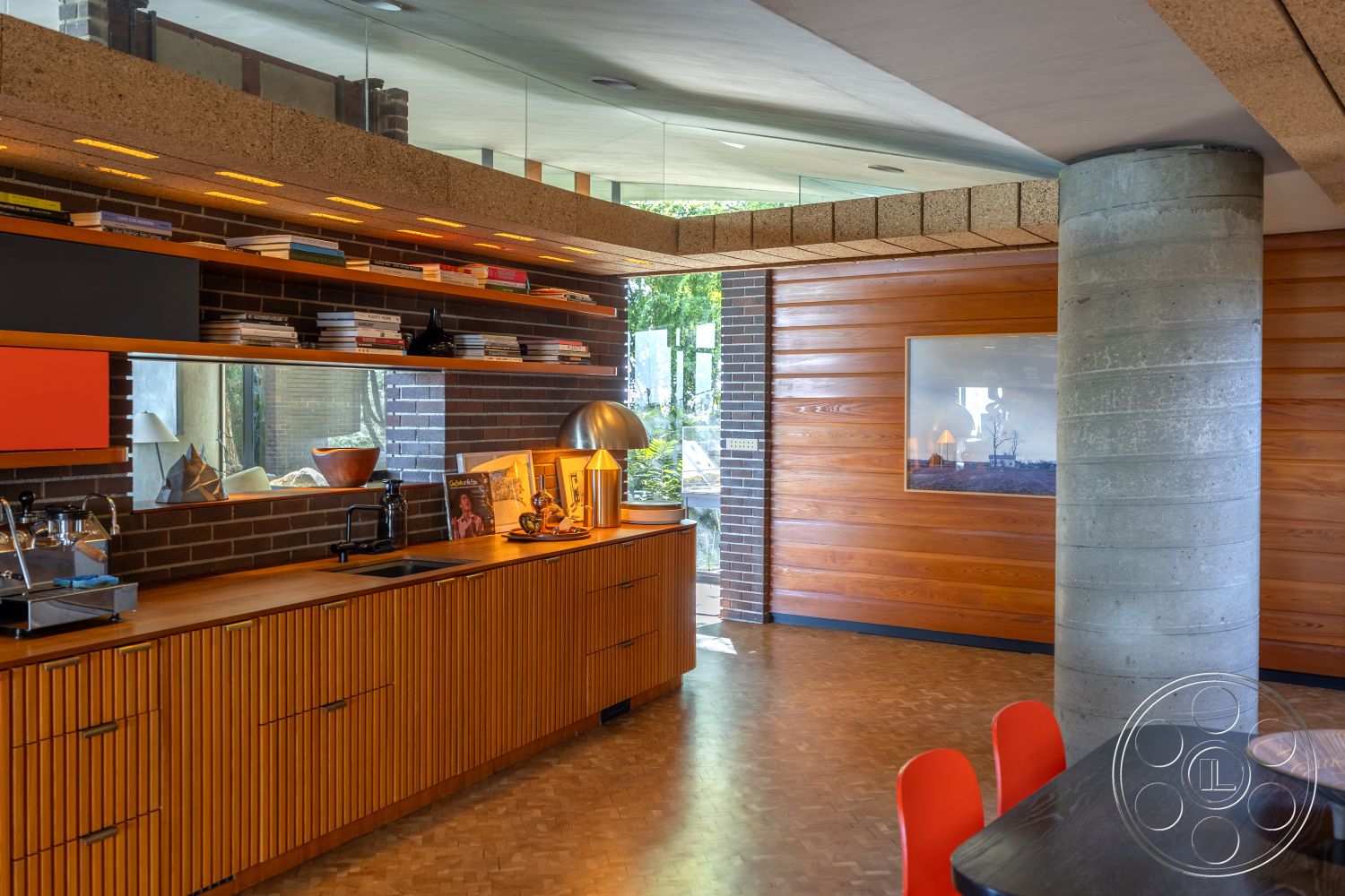 Silvertop House - minimalist design elements, modern pendant lighting, herringbone pattern flooring, natural greenery view, contemporary interior style, large glass window, exposed brick kitchen wall, laminate countertop, inviting kitchen atmosphere, integrated kitchen storage, textured ceiling design, concrete column support, wood panel kitchen cabinetry, floating shelves with books, linear pendant light fixtures, architectural cork ceiling, open plan interior layout, wood grain texture, brightly colored accent walls, multi-textured surfaces, efficient workspace layout