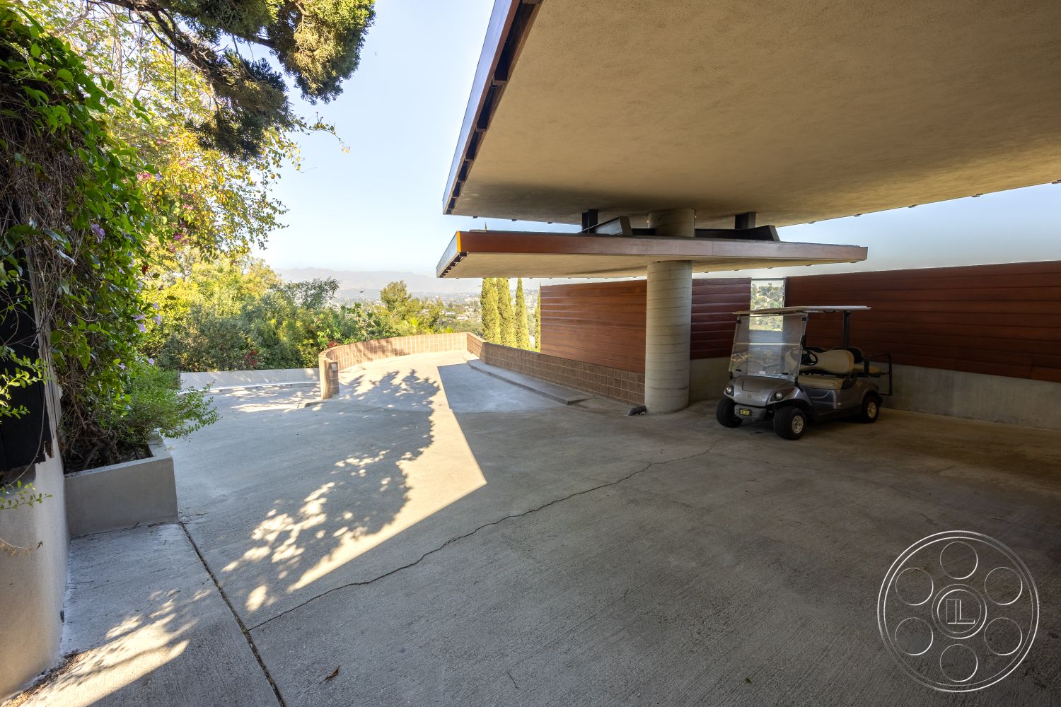 Silvertop House - exterior concrete driveway, exterior modern architectural style, exterior concrete floor, exterior concrete support columns, exterior soft natural light, exterior wood panel wall, exterior landscaped environment, exterior golf cart parking area, exterior raised patio, exterior structural overhang, exterior view of hillside setting, exterior green vegetation surrounding