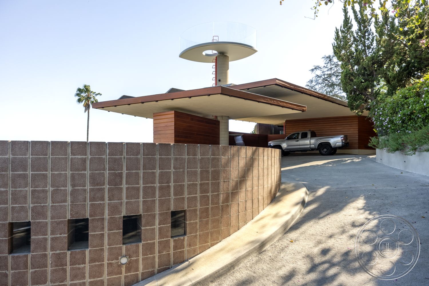 Silvertop House - landscaped garden, flat roof, architectural details, floor-to-ceiling windows, multi-level structure, concrete driveway, curved driveway, mid-century modern style, palm tree landscaping, overhanging roof eaves, outdoor patio area, urban hillside setting, wood panel siding, exterior lighting fixtures, ground-level entryway, exposed concrete block wall, modern construction, perched observation deck