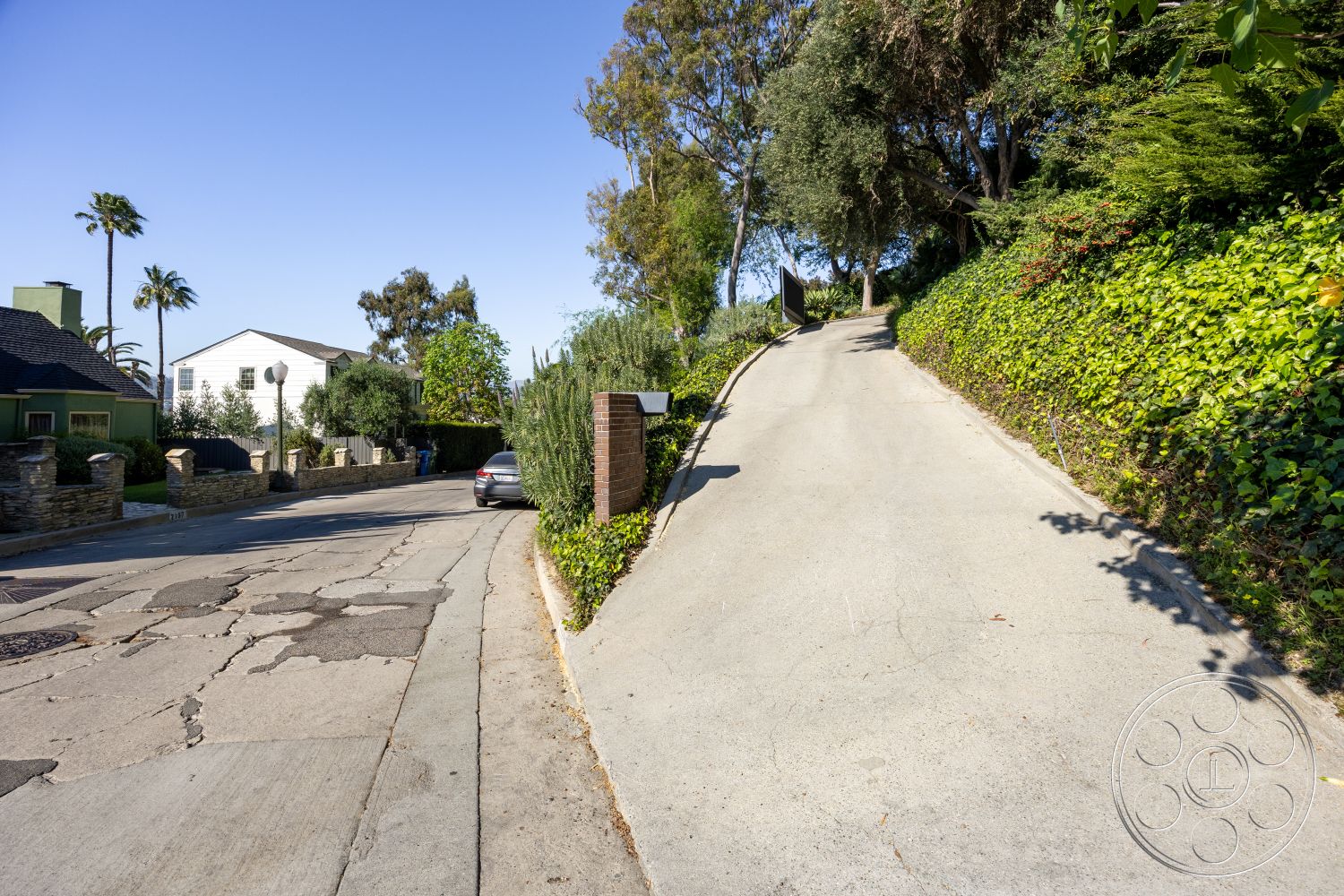Silvertop House - exterior, residential neighborhood, concrete driveway, sloped driveway, stone retaining wall, urban hillside location, asphalt road surface, tropical plant landscaping, landscaped garden borders, modern gate entrance, palm trees setting