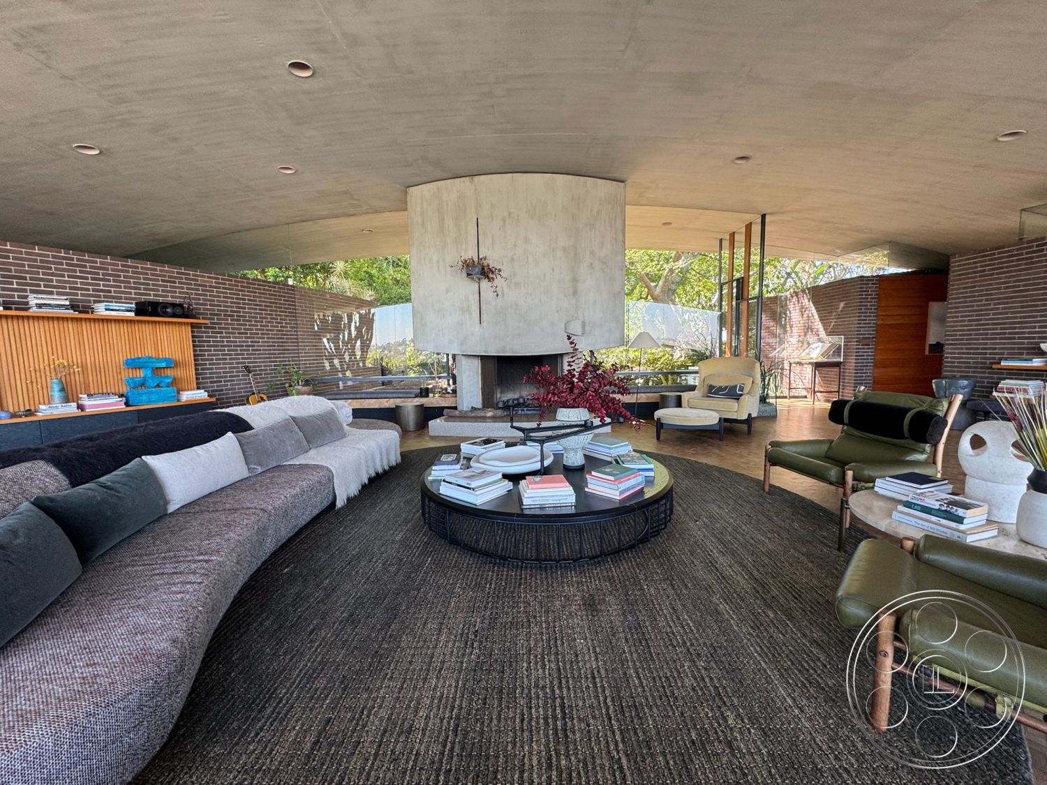 Silvertop House - textured area rug, open floor plan, indoor-outdoor flow, earthy color palette, vaulted ceiling, casual seating arrangement, curved sectional sofa, contemporary lounge area, minimalist architectural style, exposed brick accent wall, outdoor greenery view, hardwood floor in living area, glass wall with natural light, modern coffee table design, concrete interior ceiling, integrated wood shelving, floating fireplace feature, mixed material furnishings, low-profile design aesthetics