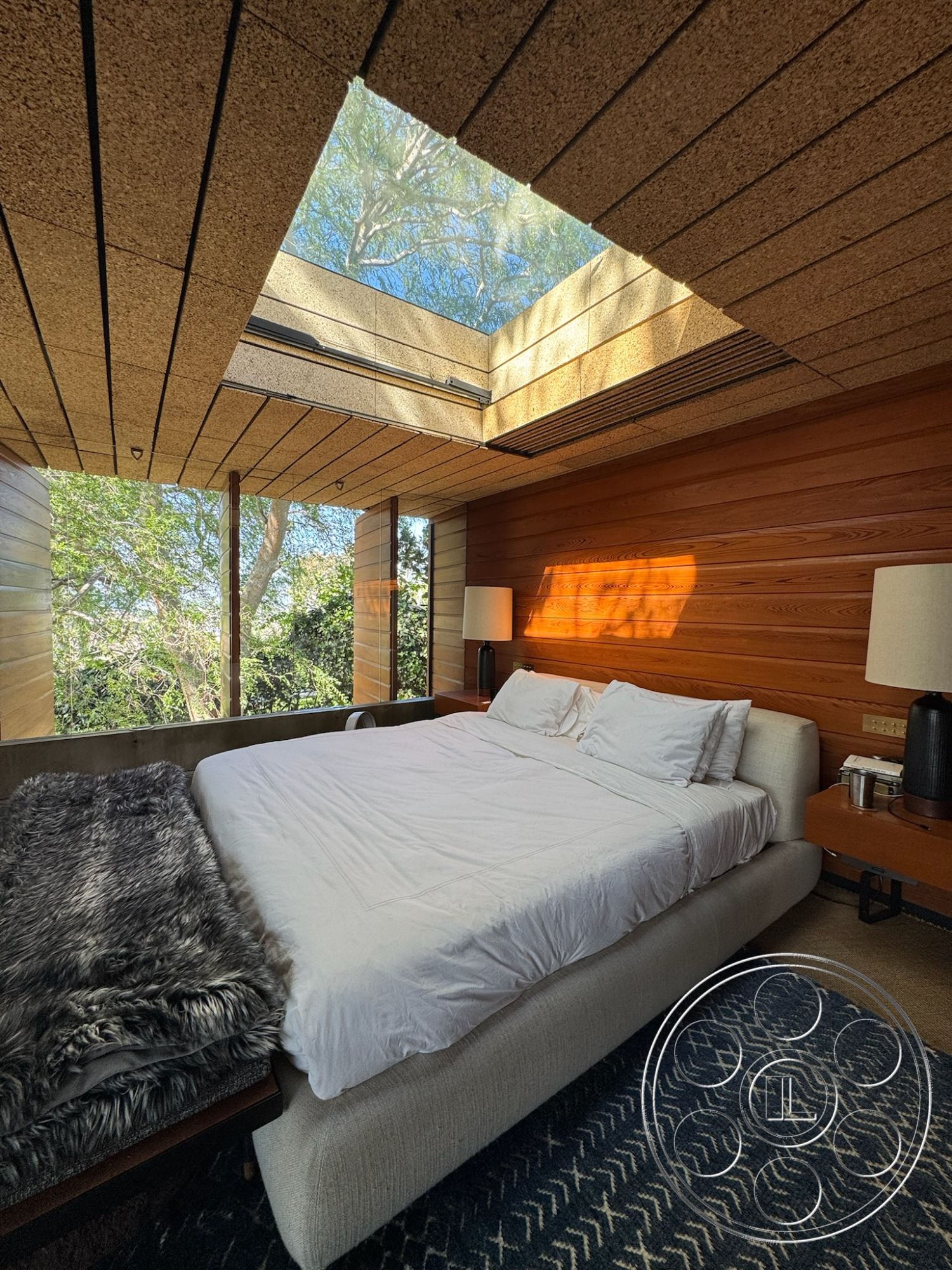 Silvertop House - minimalist decor, geometric area rug, exposed concrete ceiling, wool throw blanket, contemporary design aesthetic, interior bedroom space, natural light ambiance, wood paneling walls, skylight ceiling feature, soft-textured bedding, large windows with nature view, hardwood bedside tables