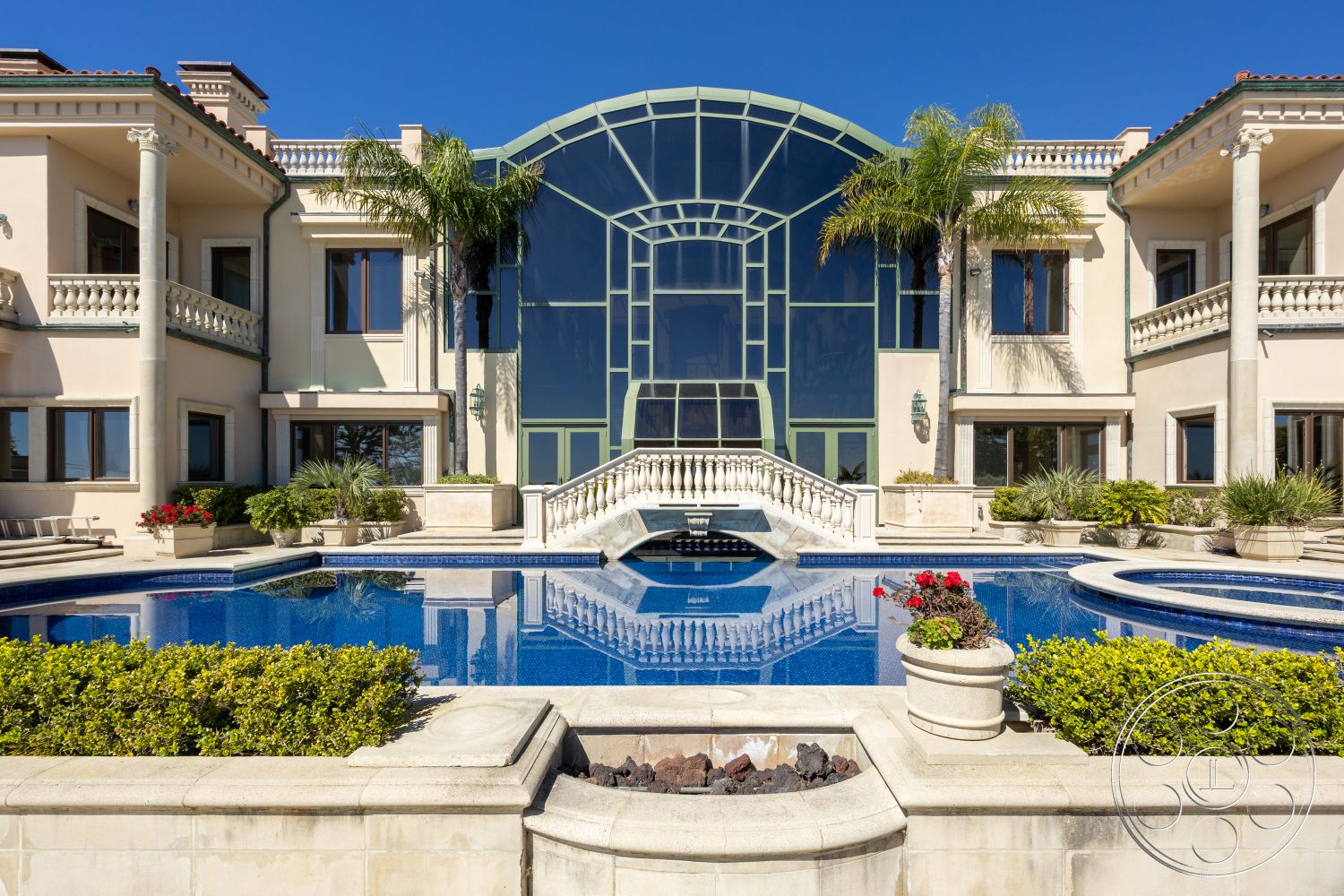 Pacifica Estate - rectangular swimming pool, glass patio doors, infinity edge pool, outdoor relaxation area, arched entryway, floor-to-ceiling glass windows, built-in seating area, luxurious outdoor living space, landscaped garden with palm trees, landscaped poolside garden, stucco wall finishes, classical architectural details, paver pool deck, elegant stone pool border, glass railing accents, balustrade terrace, granite stone fire pit, marble decorative planter pots, Mediterranean villa style