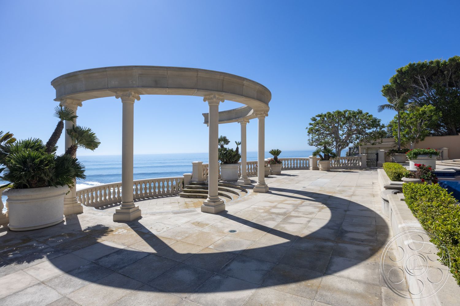 Pacifica Estate - circular design elements, palm landscaping, terraced garden design, oceanview setting, exterior marble patio flooring, exterior stone column support, curved pergola structure, sunny coastal terrace, ornamental flower planters, shadow play on stone surface