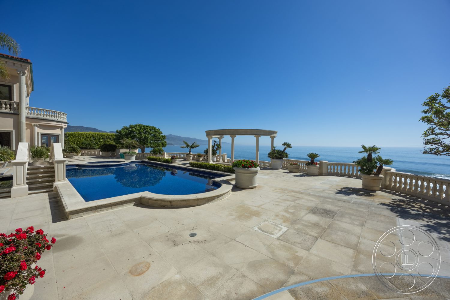 Pacifica Estate - stucco walls, infinity pool, coastal setting, rectangular pool, Mediterranean architectural style, stone pool deck, exterior concrete patio floor, oceanfront view, balustrade railing, landscaped garden with planters, columned gazebo, brick planter borders, concrete steps leading to the pool, potted palm trees, sunny outdoor lounging area