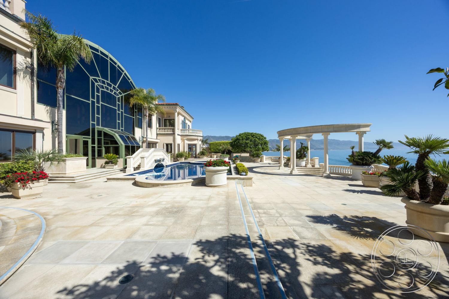 Pacifica Estate - luxurious outdoor setting, rectangular pool shape, panoramic ocean view, urban hillside location, contemporary architectural details, exterior concrete patio flooring, infinity pool with tiled waterline, curved pool deck with stone coping, arched colonnade with decorative columns, modern glass wall feature, landscaped terrace with tropical plants, potted garden with palm trees, multilevel outdoor living space, expansive terrace for entertaining