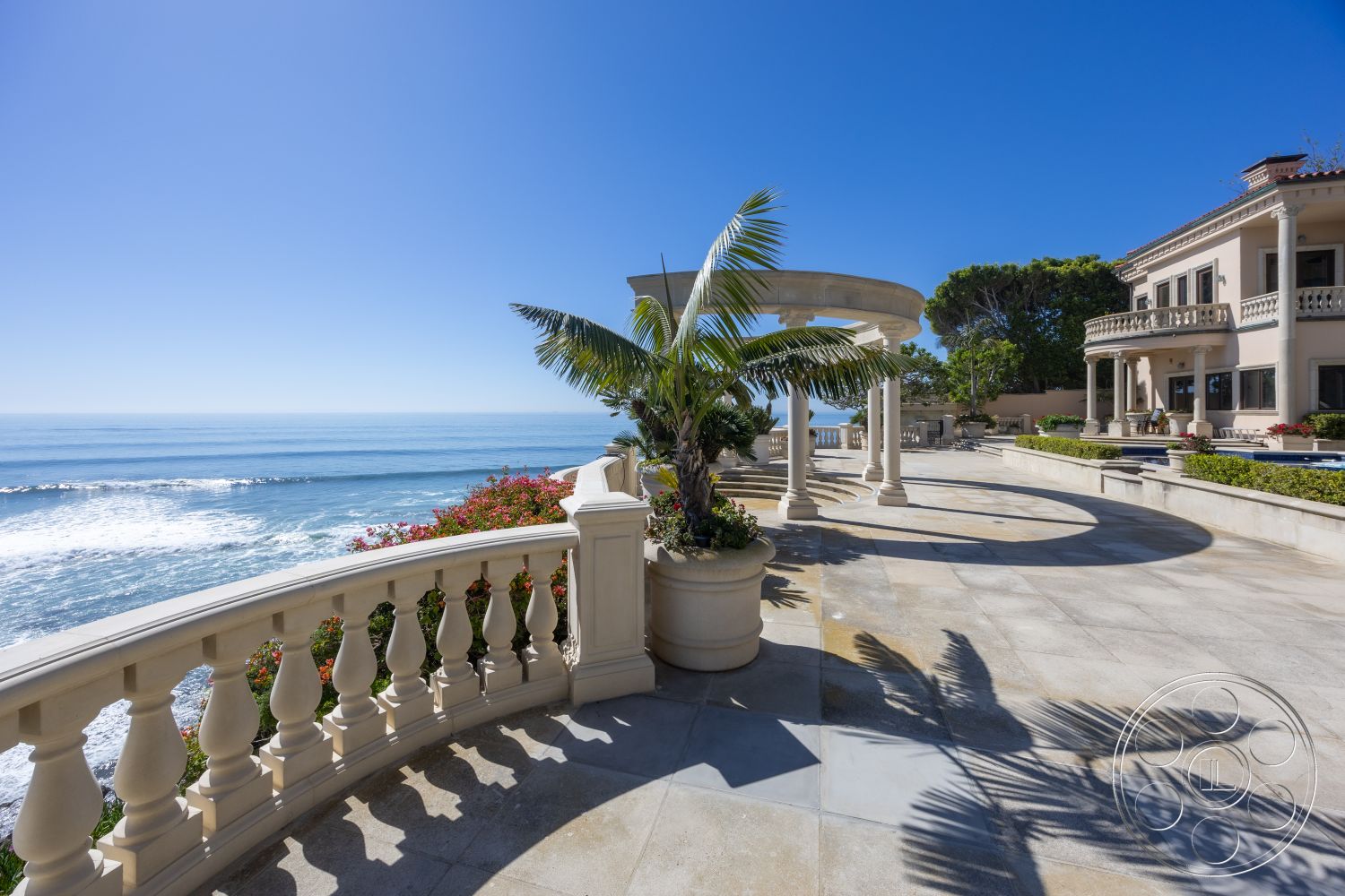 Pacifica Estate - large windows for natural light, palm trees landscape, luxury outdoor living space, exterior patio flooring, decorative flower beds, surrounding coastal environment, limestone pool deck, curved stone railing, expansive oceanfront view, modern Mediterranean villa architecture, outdoor columns with rounded tops, clean lines architectural detail, beautiful coast view