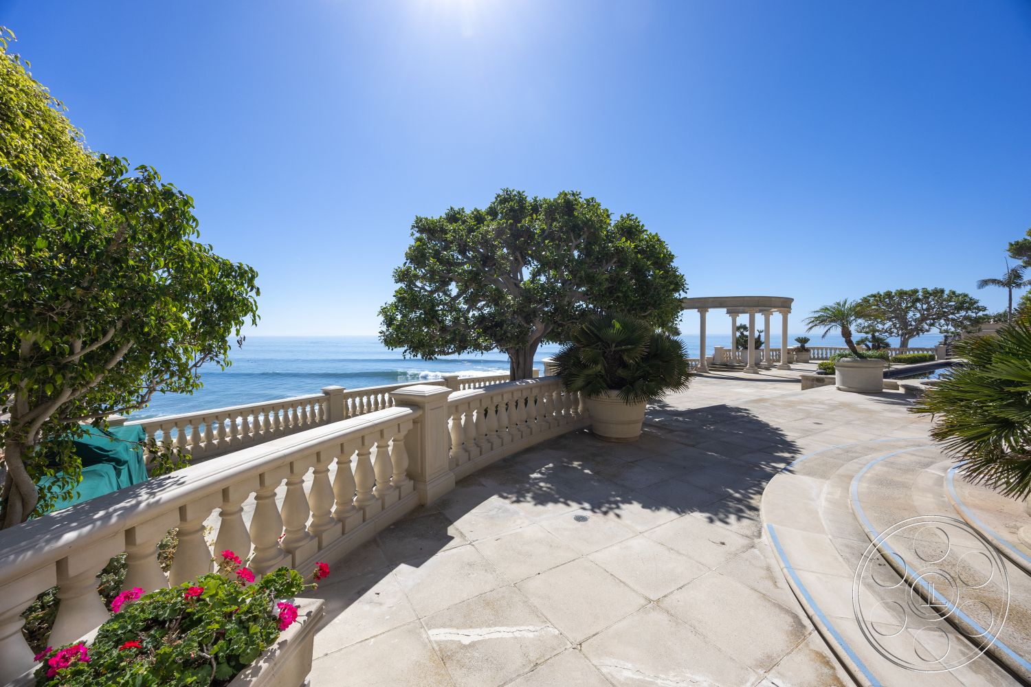 Pacifica Estate - oceanfront property, coastal landscape setting, smooth concrete steps, landscaped outdoor space, rectangular pavers, blue sky backdrop, exterior marble patio flooring, curved stone balustrade, tropical garden planters, palm trees in the garden, white columned pergola, uninterrupted sea view, sunny beachside terrace, horizontal railing design, serene waterfront ambiance