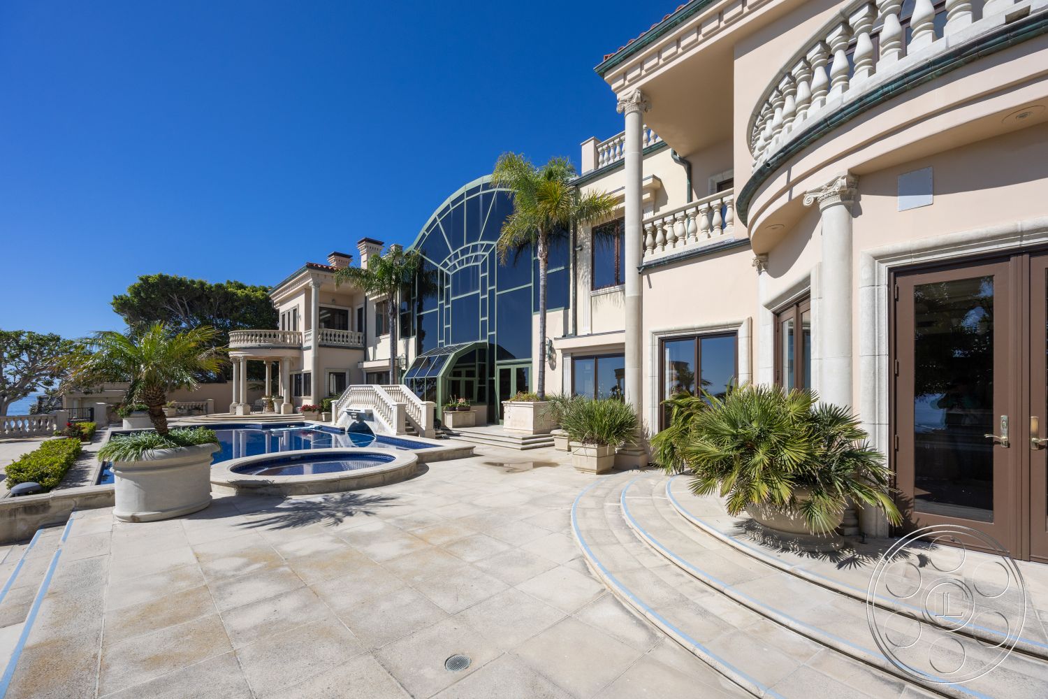 Pacifica Estate - exterior, large glass doors, rectangular swimming pool, outdoor living space, modern architectural style, luxury home, seaside view, stone pool deck, concrete steps leading to pool, built-in planters, urban beachfront setting, marble patio flooring, contemporary exterior details, multiple outdoor seating areas, glass arch windows, ornamental stone balustrades, landscaped garden area with palm trees, vaulted patio ceiling, curved patio edges, detailed stone façade