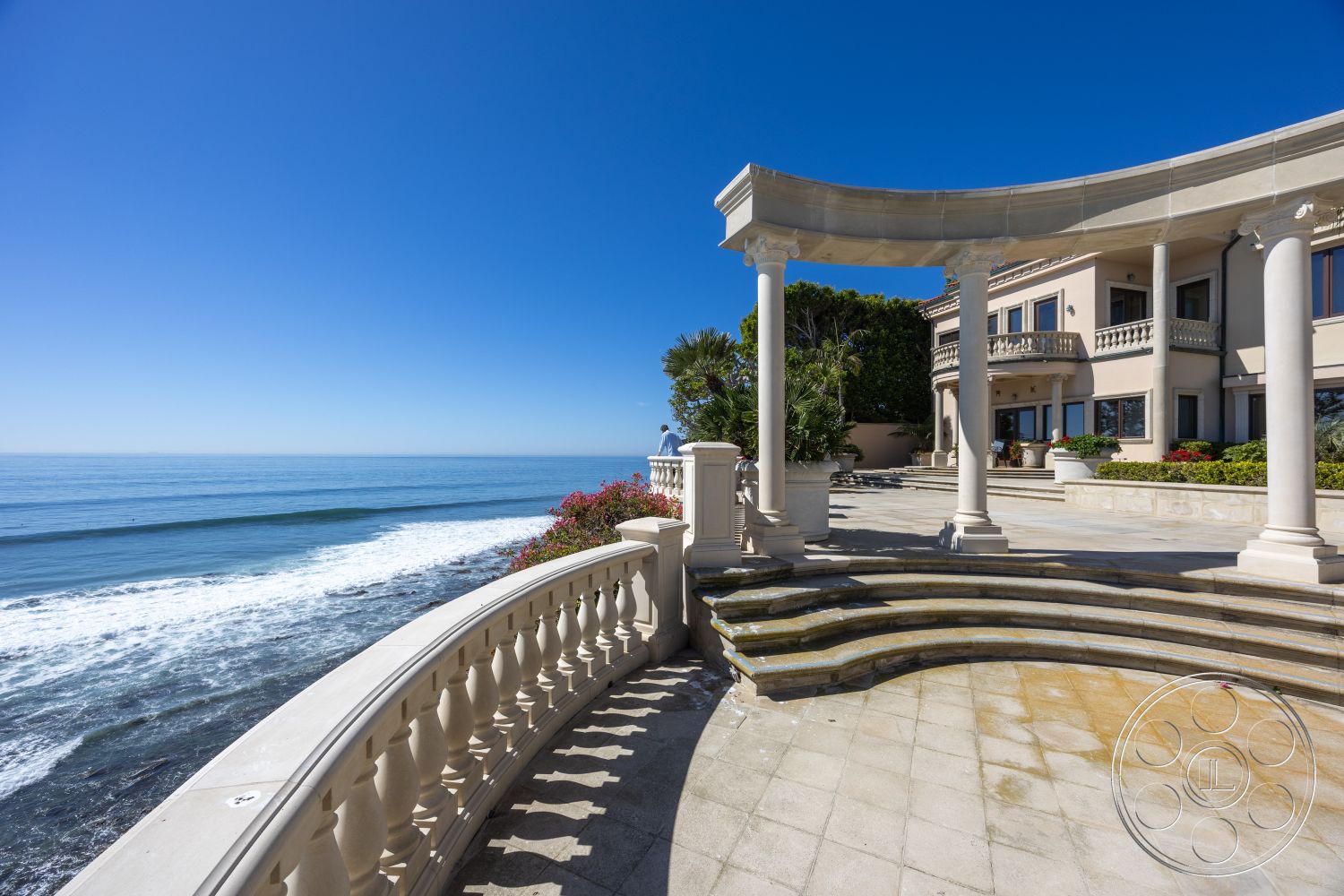 Pacifica Estate - arched doorways, open-air terrace, pillared entrance, landscaped garden area, stucco wall finish, curved patio design, two-story Mediterranean home, concrete balustrade railing, exterior patio flooring, coastal oceanfront view, glass window wall, oval pool deck stone, marble outdoor steps, hardscape border plants, floor-to-ceiling sliding doors