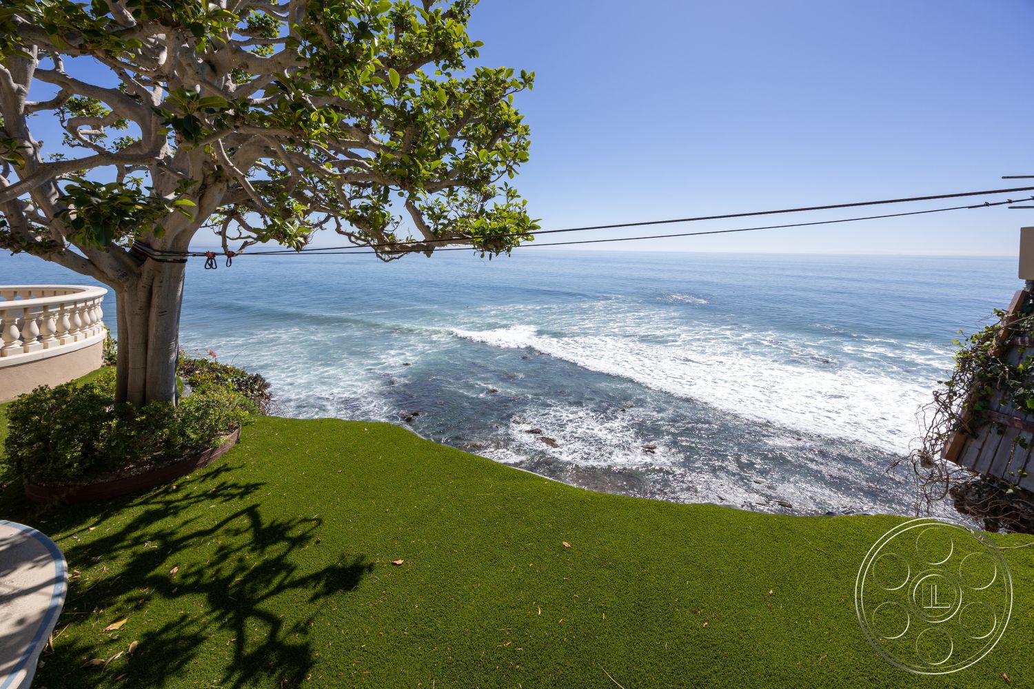 Pacifica Estate - clear blue sky, beachfront property, ocean view setting, landscaped garden exterior, artificial turf lawn exterior, balustrade edge detail, coastal landscape environment, tree shade area, seaside property, sunny coastal platform, green lawn with ocean backdrop, nautical horizon line, tropical tree line, rocky shoreline view, open space coastal area
