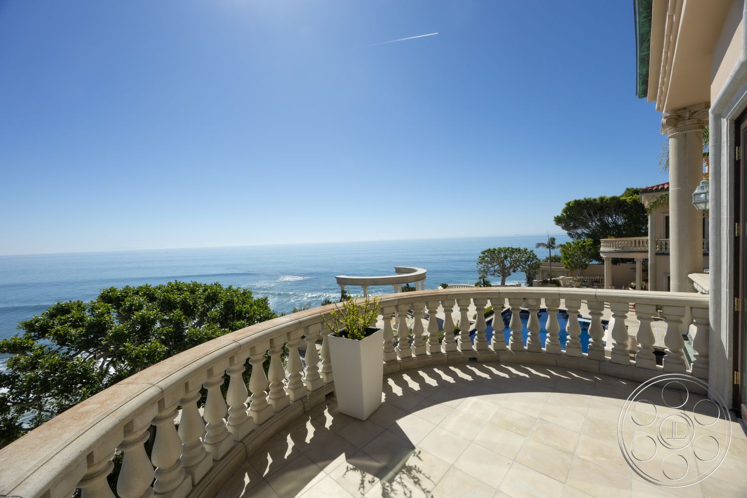 Pacifica Estate - contemporary design elements, clear blue sky, smooth stone surfaces, elegant architectural details, stone patio flooring, oceanfront property, panoramic sea view, decorative stone balustrade, curved balcony railing, sunlit outdoor space, tile patio flooring, open-air balcony, exterior balcony with ocean view, spacious outdoor terrace, lush landscape with greenery, coastal living environment, surrounded by tropical vegetation, luxurious seaside retreat, exquisite outdoor entertaining area, stylish outdoor planters