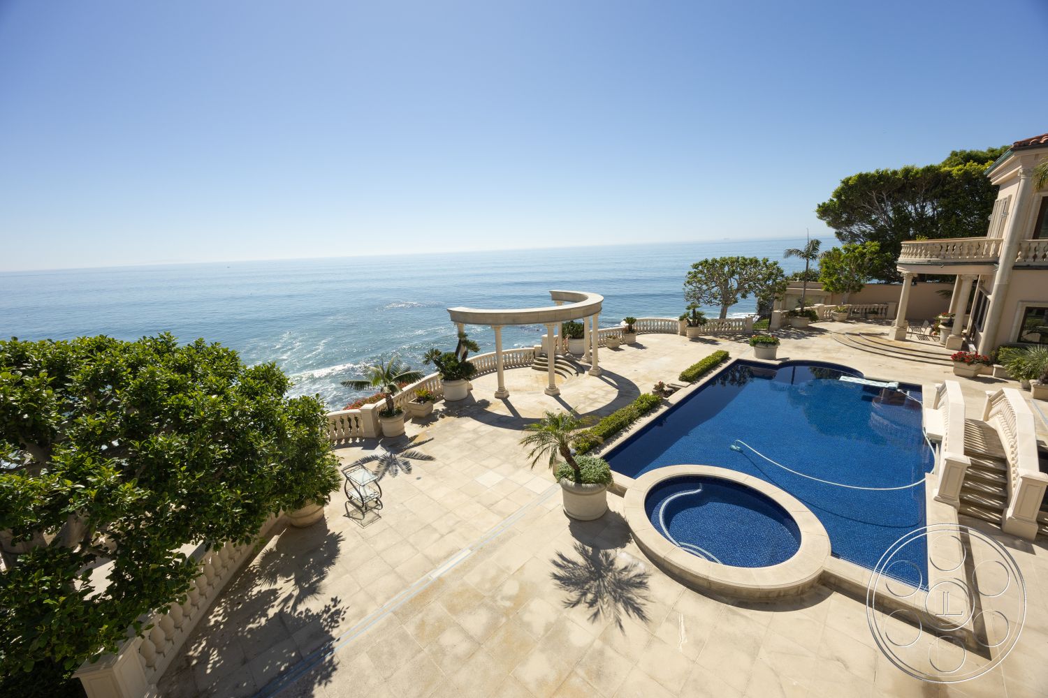 Pacifica Estate - exterior, outdoor seating area, rectangular swimming pool, tropical landscaping, coastal view, terraced landscaping, stone patio flooring, oceanfront property, weather-resistant outdoor furnishings, mediterranean architectural style, limestone pool deck, potted palm trees, kidney-shaped spa, overhead pergola, colonnade with archways, curved steps leading to pool